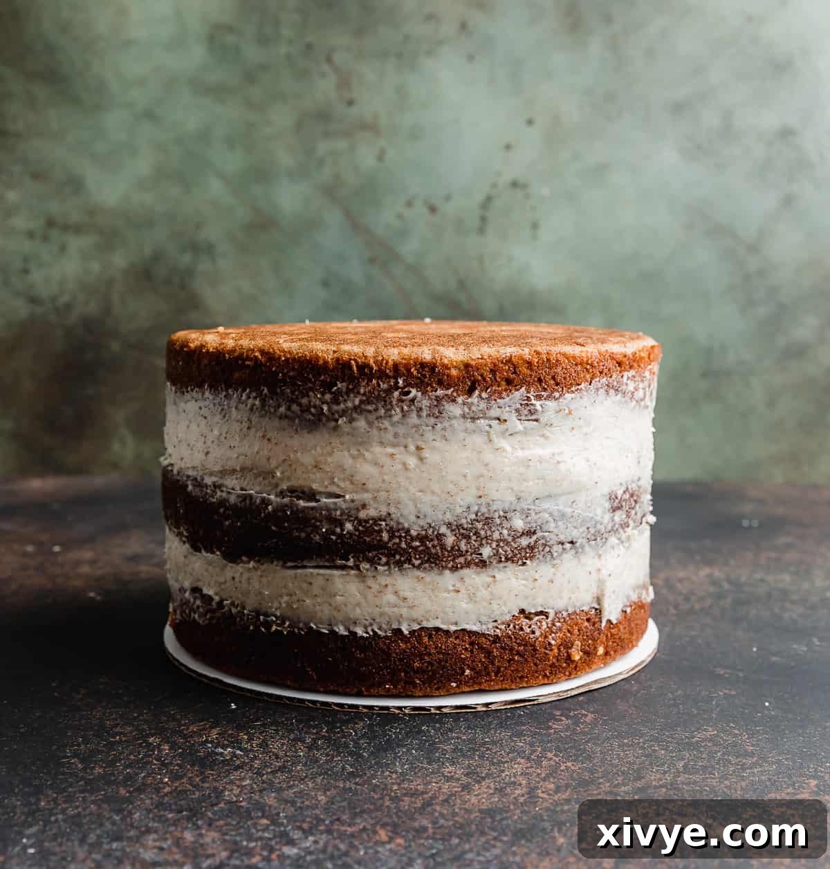 Sunshine Pineapple Pecan Carrot Cake 7 A three layer moist carrot cake recipe covered in a crumb coat, against a textured green and brown background.