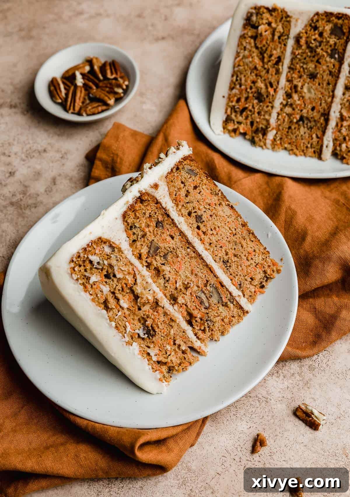 Sunshine Pineapple Pecan Carrot Cake 10 A slice of three layer Carrot Cake with cream cheese frosting on a white plate on a burnt orange linen napkin.