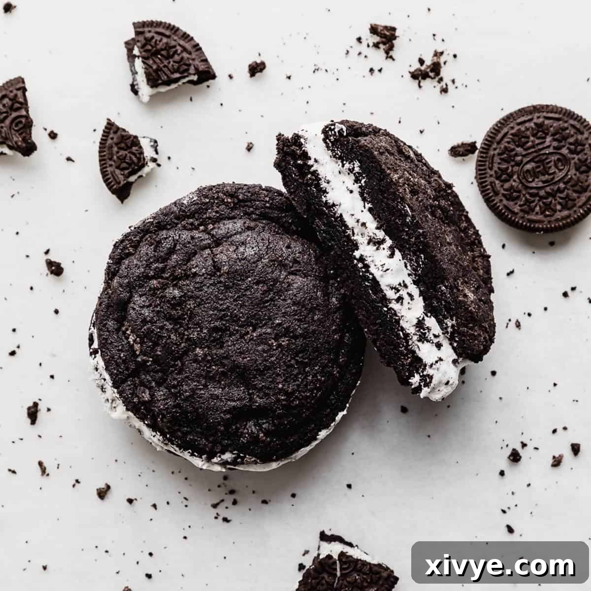 A perfectly crafted copycat Crumbl Oreo sandwich cookie, artfully placed on a pristine white background, surrounded by scattered Oreo crumbs.
