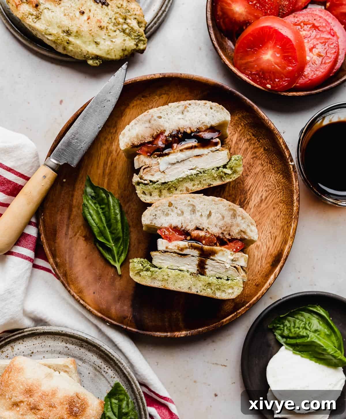 Gourmet Caprese Chicken Sandwich 2 A Chicken Caprese Sandwich topped with tomato, mozzarella, pesto, and balsamic glaze on a round brown plate, inviting diners to savor its fresh ingredients.