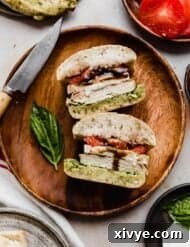 A Chicken Caprese Sandwich Recipe on a brown wooden plate on a beige background with a red and white stripe napkin to the side of the plate.