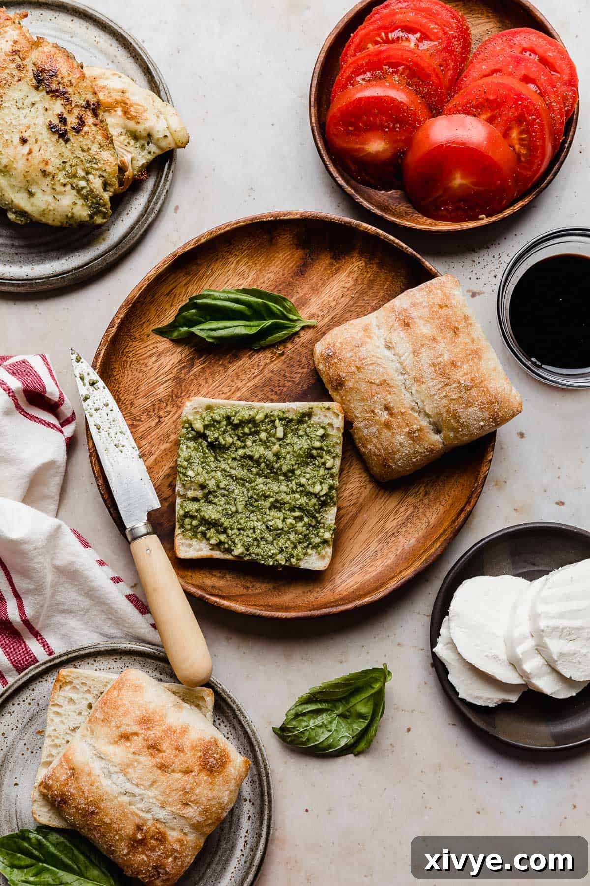 Gourmet Caprese Chicken Sandwich 4 A round wooden plate with a slice of artisan bread on it that has basil pesto smeared overtop, ready for assembly.