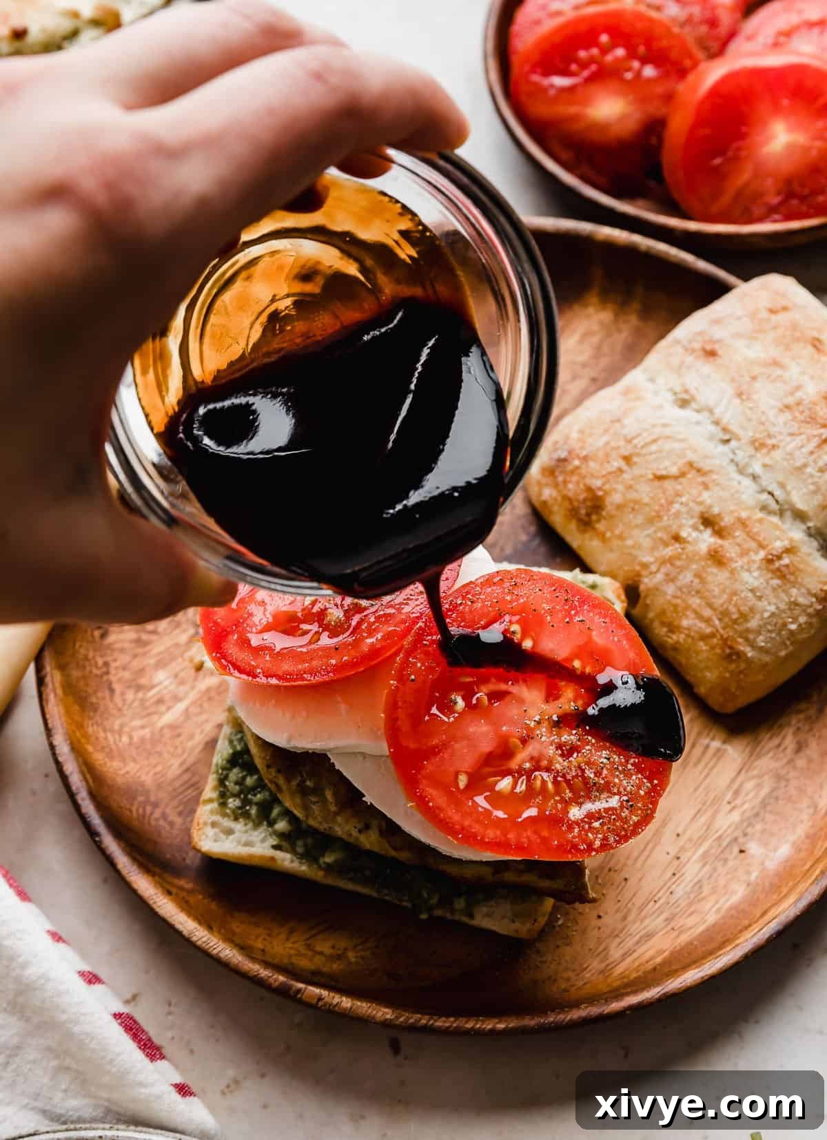 Gourmet Caprese Chicken Sandwich 8 Balsamic glaze being poured overtop sliced tomatoes on a Chicken Caprese Sandwich, creating a beautiful and flavorful finish.