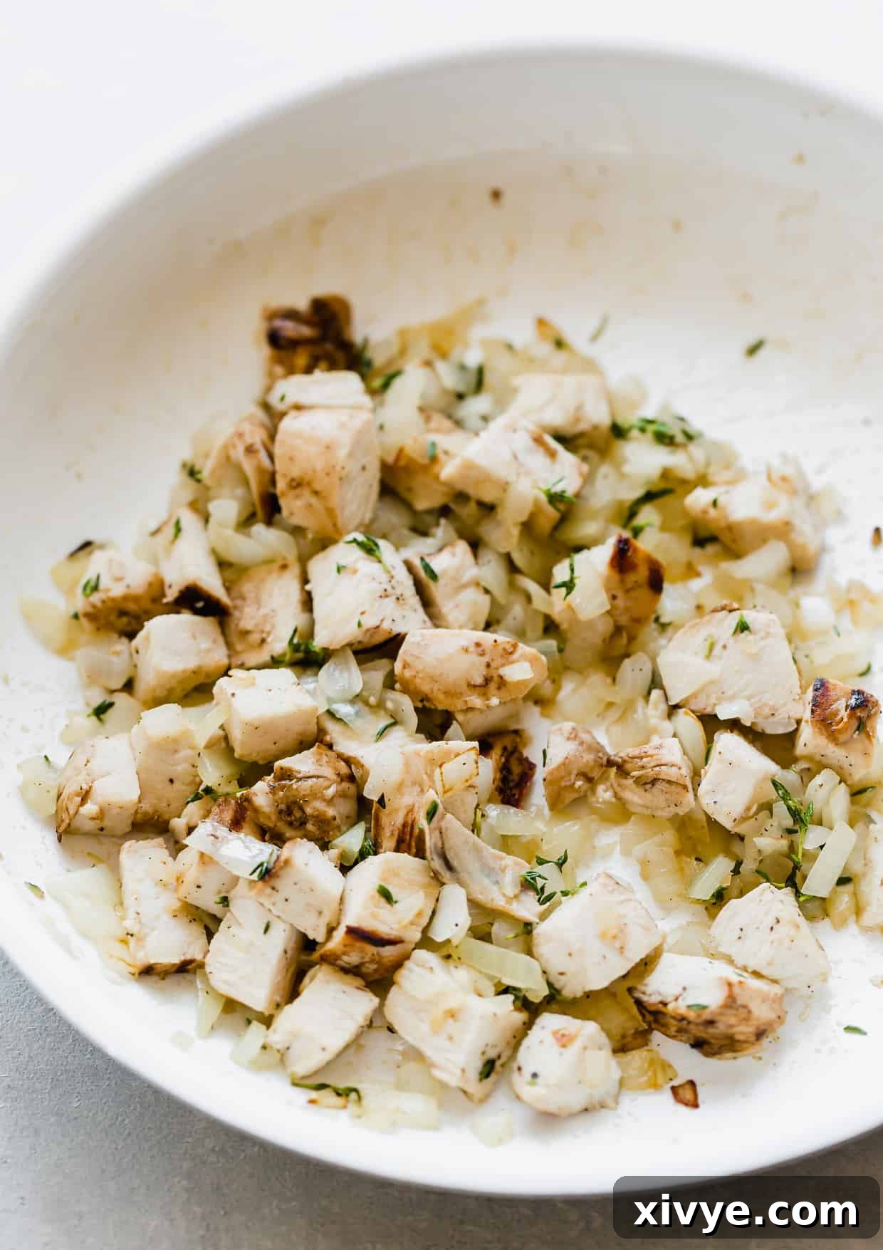 Peppery Rocket Pesto Pizza 4 A white saute pan with diced chicken, onions, and fresh thyme.