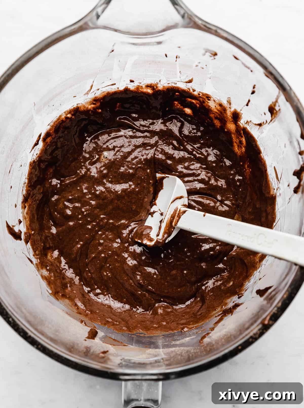 Ferrero Rocher Cupcake batter and a white spatula in a glass bowl on a white background.