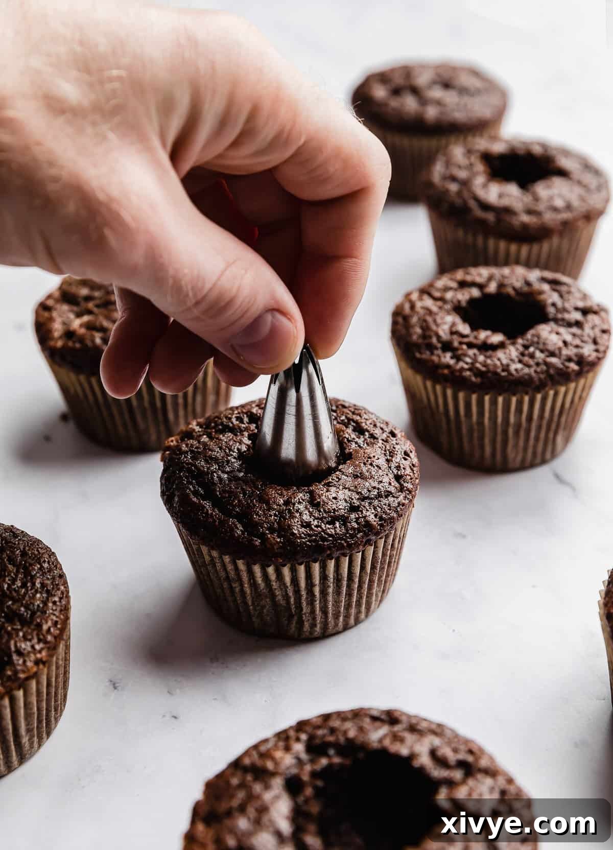 A hand using a piping tip to remove the core of a chocolate cupcake.
