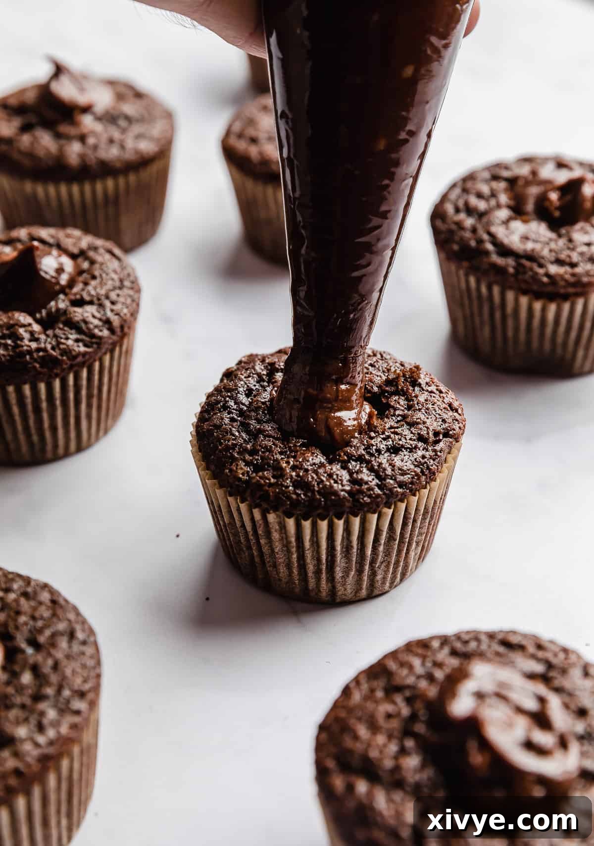 A piping bag filled with Nutella that's being dispensed into the center of a chocolate cupcake.