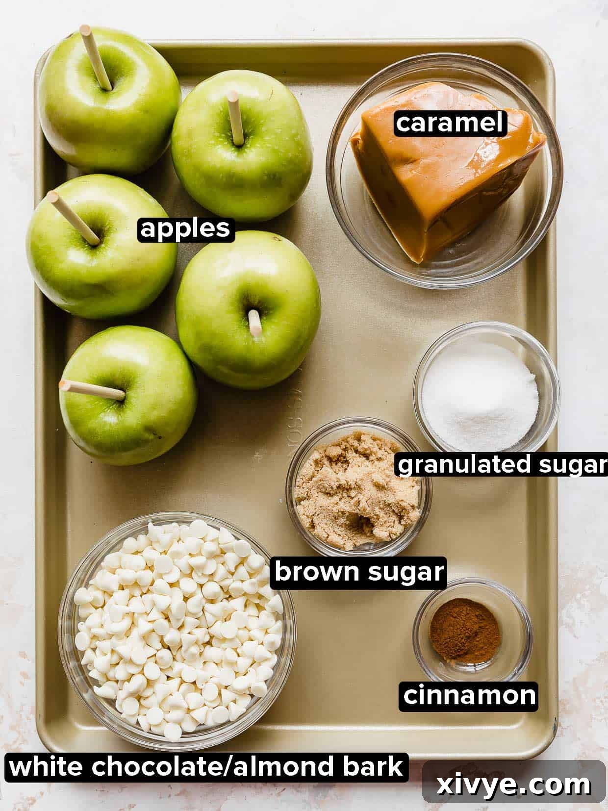 Caramel Apple Pie Fusion 3 Rocky Mountain Chocolate Factory Apple Pie Caramel Apple ingredients on a bronze baking sheet: apples, white chocolate, caramel, cinnamon, sugar, and brown sugar.