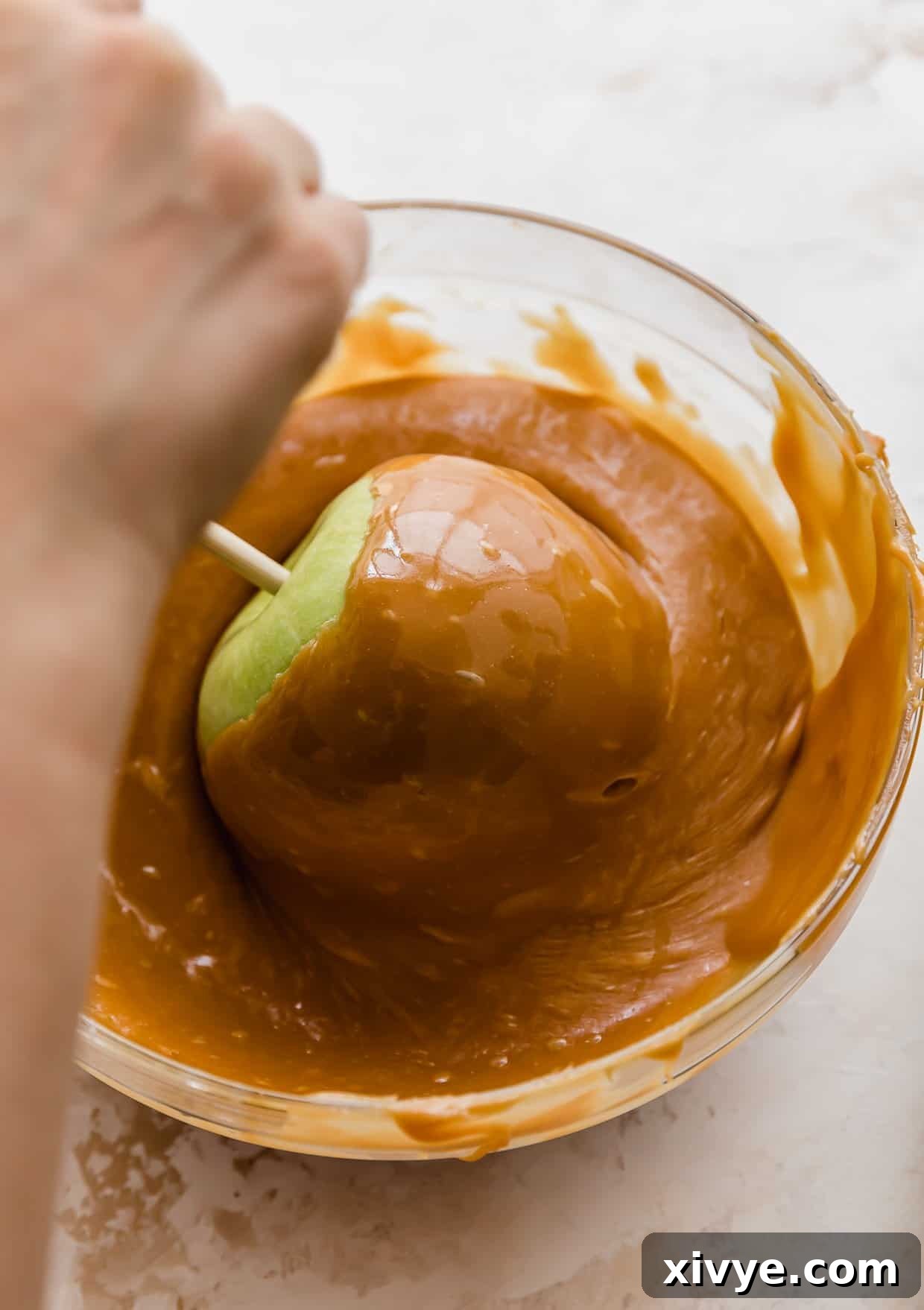 Caramel Apple Pie Fusion 7 A hand twisting a green Granny Smith apple in a bowl of caramel.