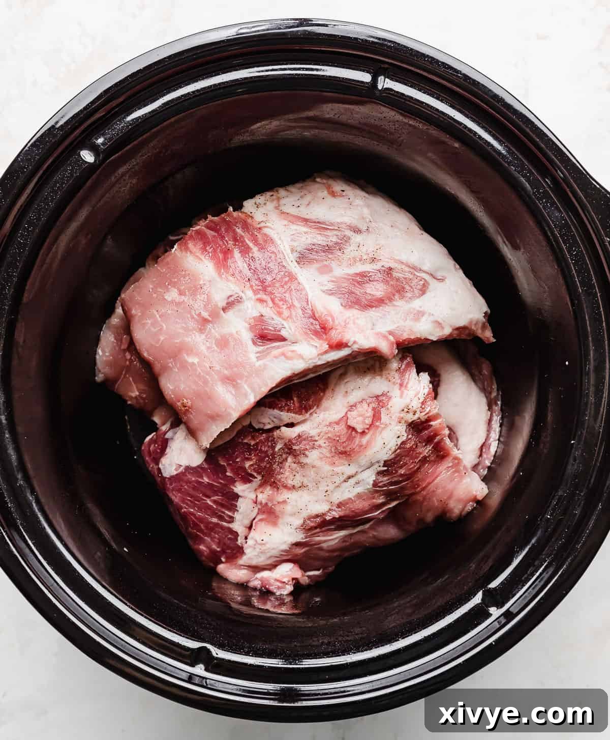 Uncooked baby back pork ribs neatly arranged in a black round slow cooker, ready for the sauce.