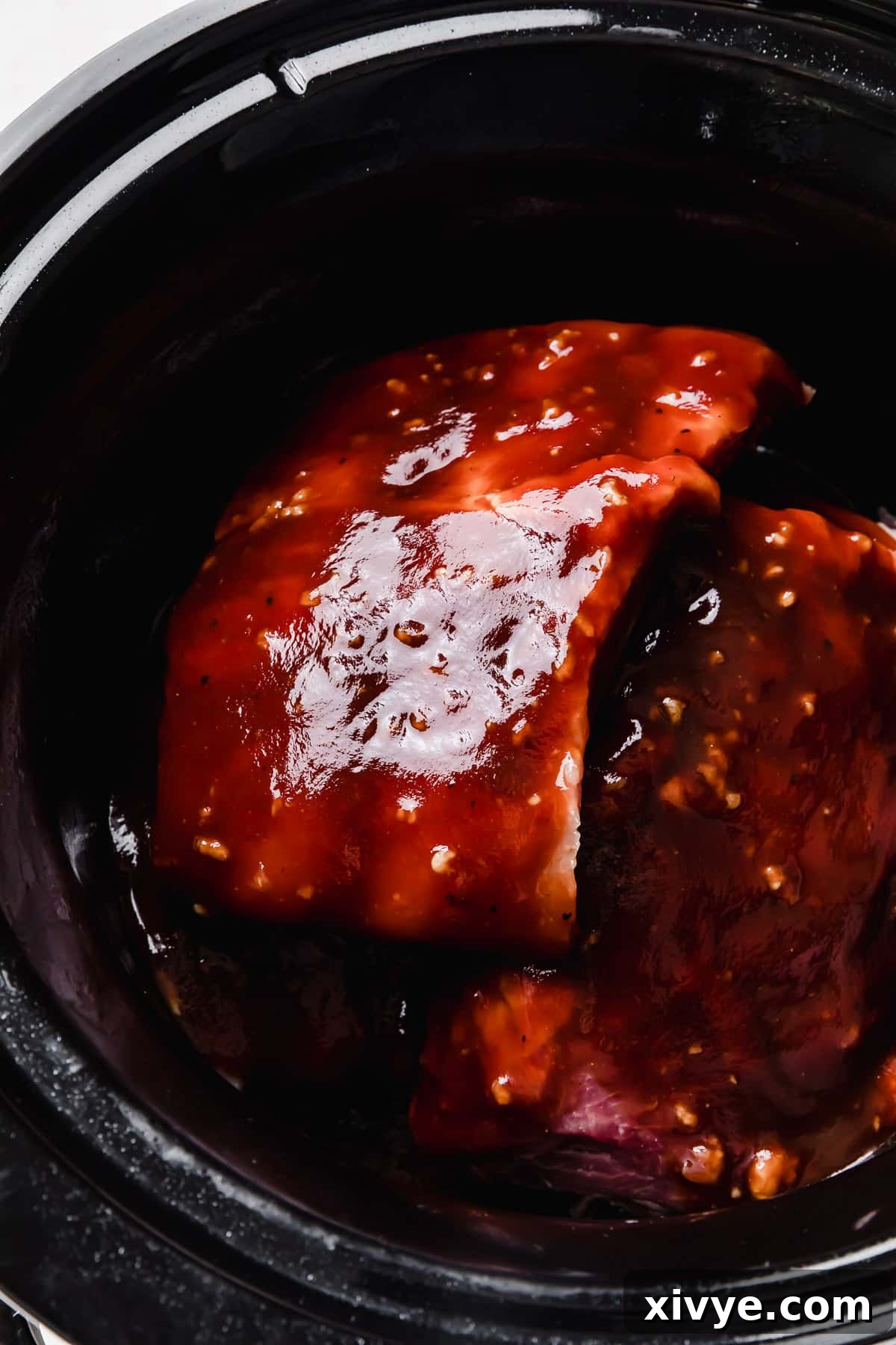 Baby back pork ribs fully covered in a rich, dark brown and red Coca Cola barbecue sauce within the slow cooker.