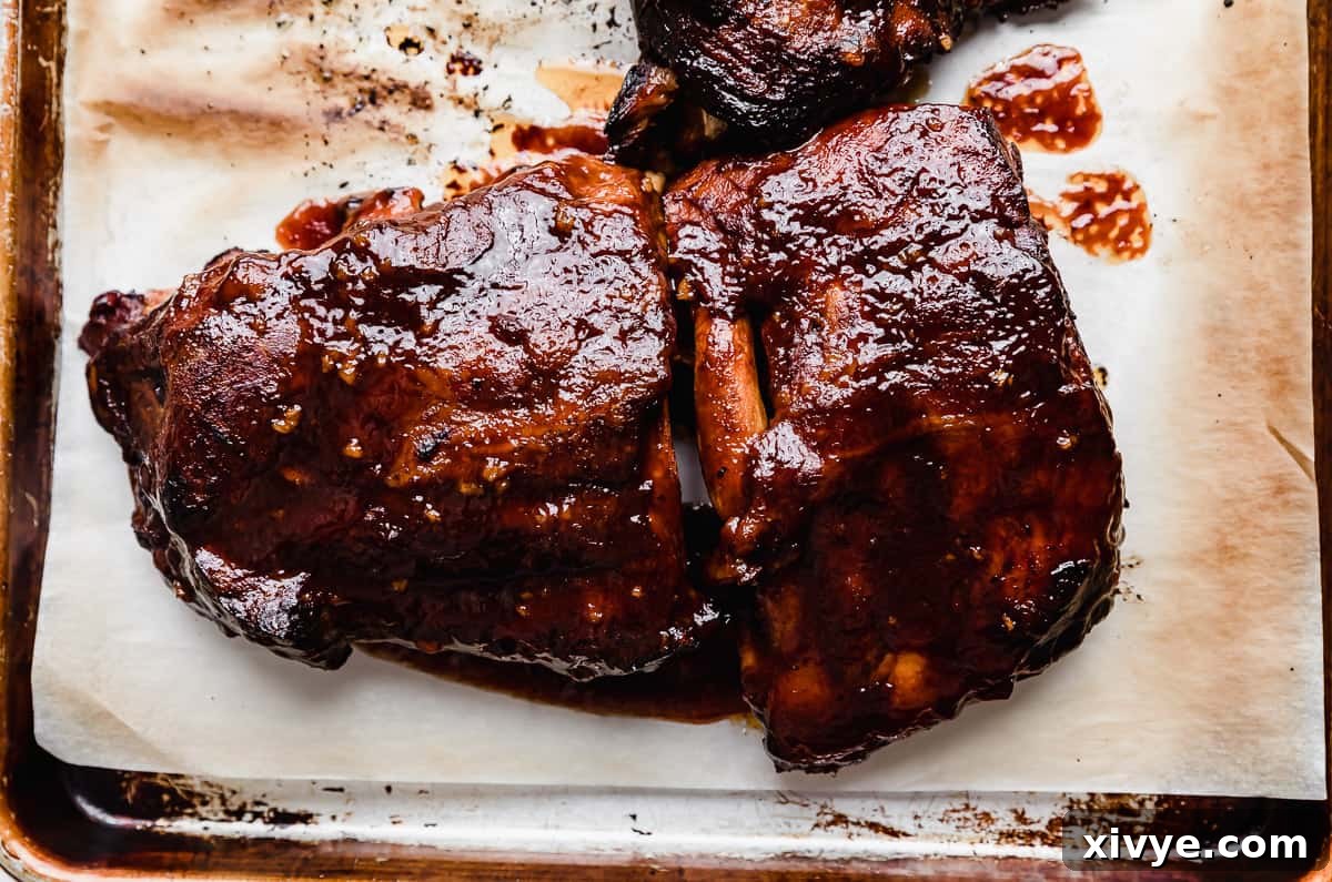 Charred Coca Cola Ribs, slow-cooked to perfection, arranged on a baking sheet lined with parchment paper, showcasing their caramelized glaze.