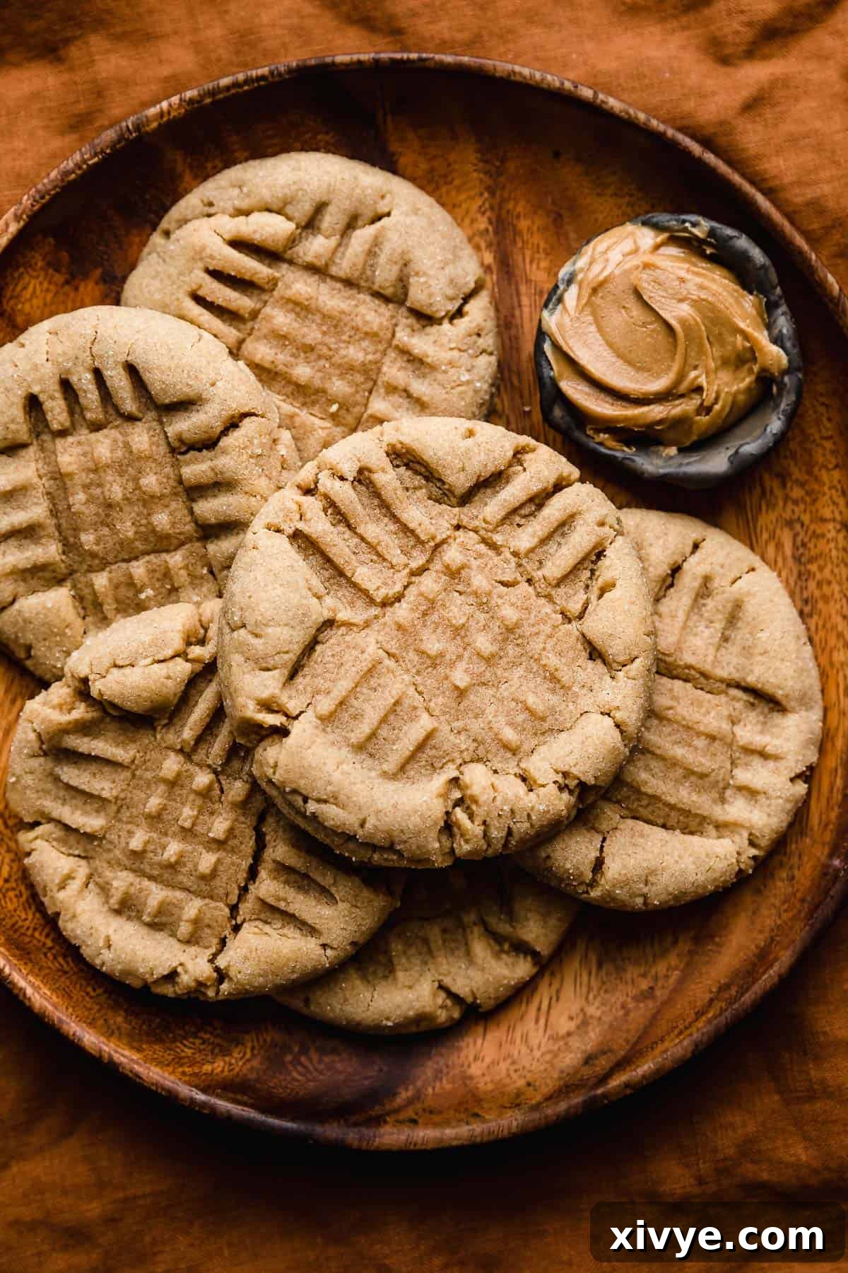 Crumbl's Iconic Peanut Butter Perfection 8 Several criss cross imprinted Peanut Butter Cookies on a round wooden plate on an amber colored background.