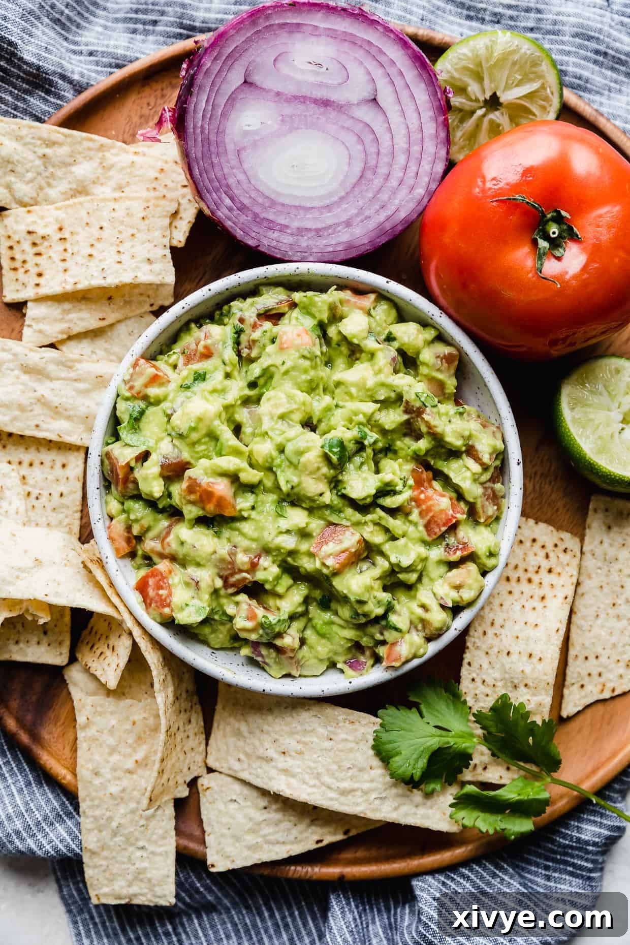 A bowl of the best guacamole on a wooden tray with tortilla chips surrounding it.