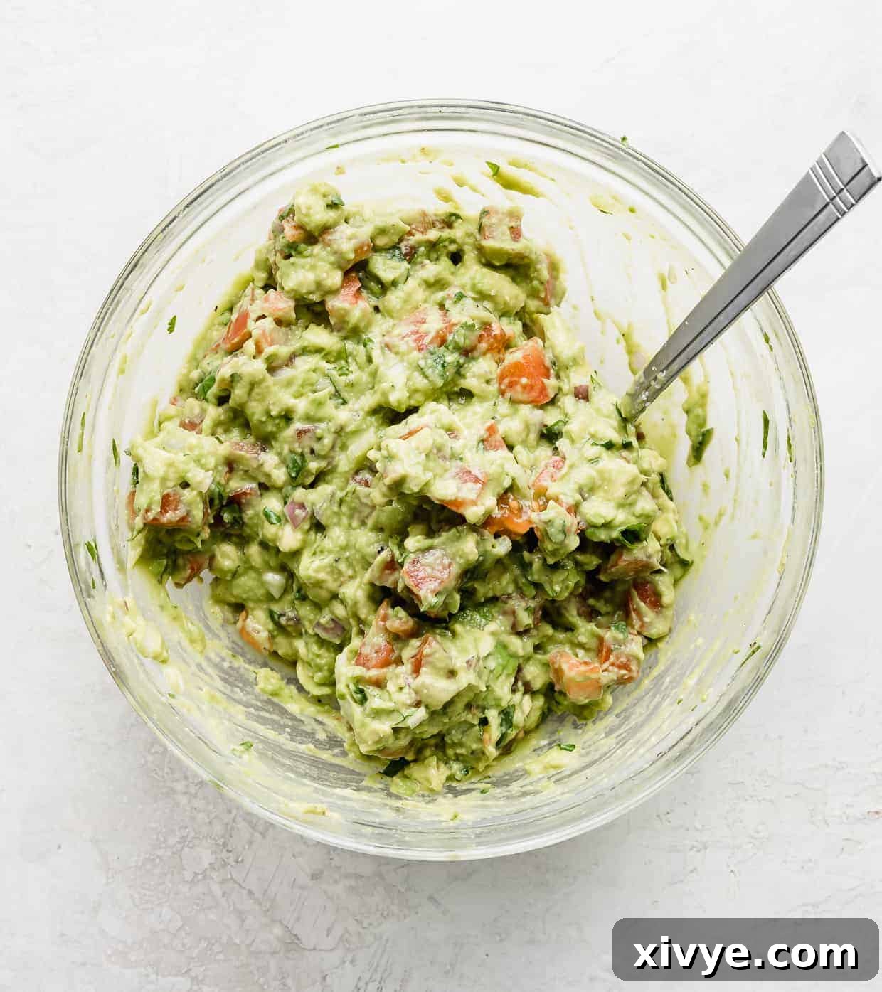 A glass bowl full of the Best Guacamole Recipe against a white background.