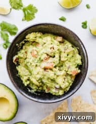 Bowl of guacamole surrounded by tortilla chips, cilantro, and limes.