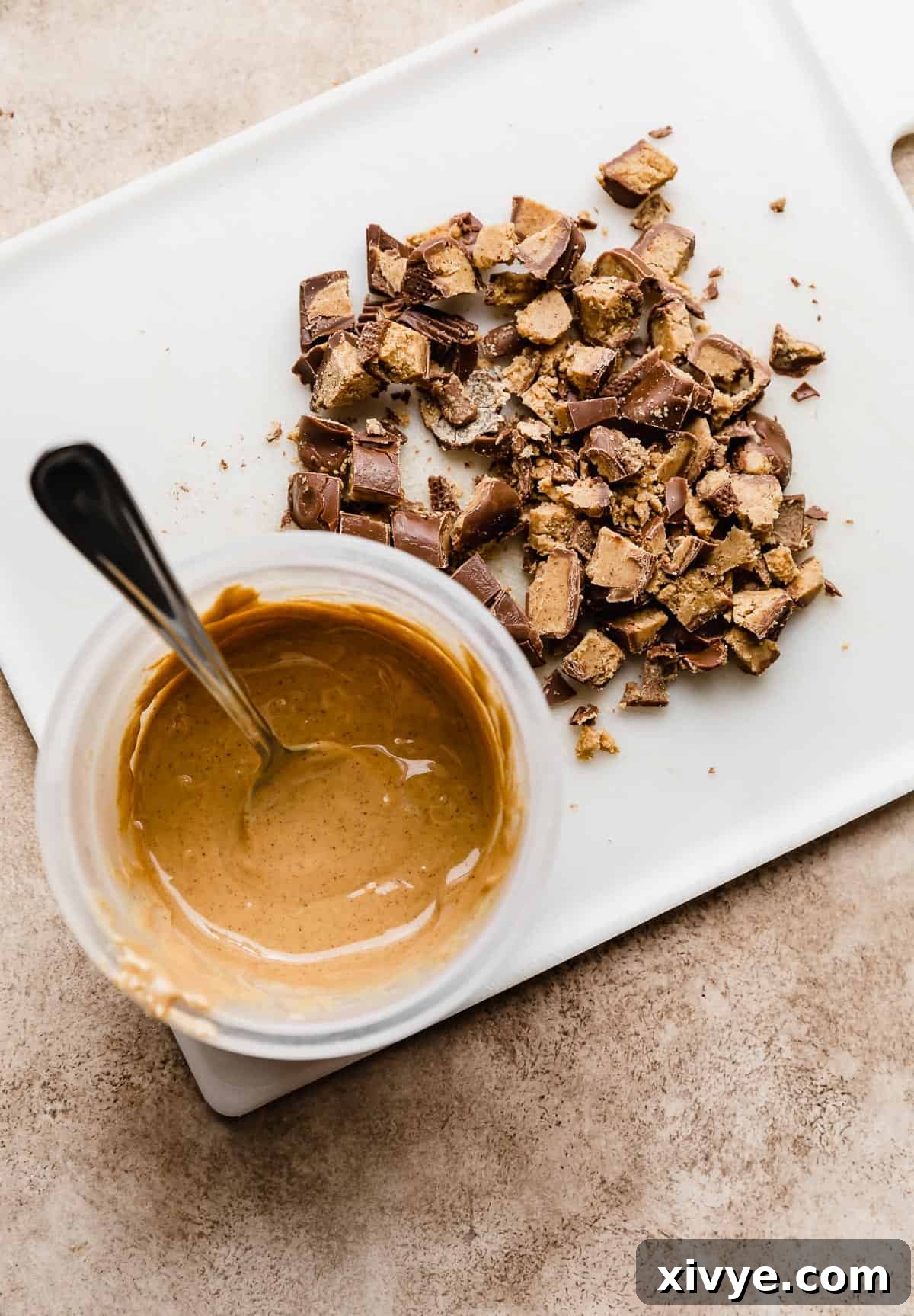 A clear glass bowl containing smooth melted peanut butter is positioned to the left, with an assortment of chopped Reese's peanut butter cups arranged neatly to its right.