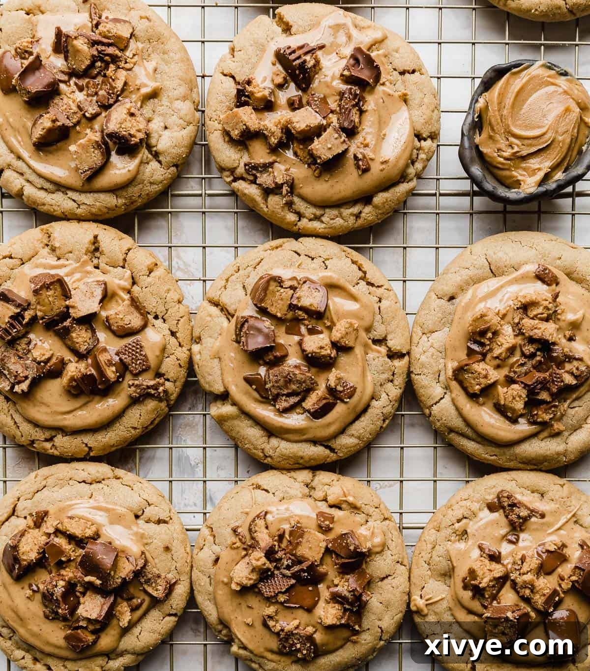 A pristine row of finished Crumbl Peanut Butter Cup Cookies resting on a wire rack, set against a clean white background, showcasing their irresistible toppings.
