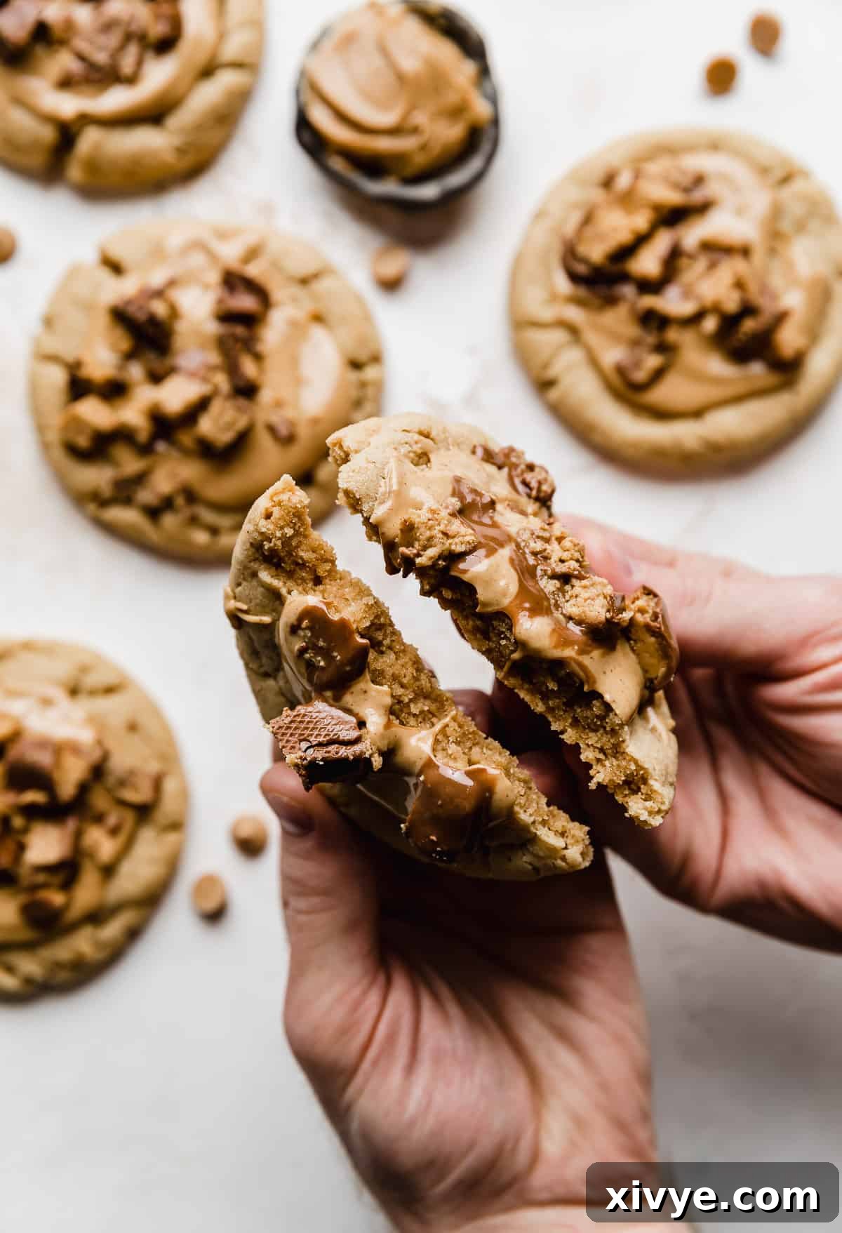 A pair of hands gently breaking a warm, copycat Crumbl Peanut Butter Cup Cookie in half, revealing its soft, chewy interior and delectable layers of topping.