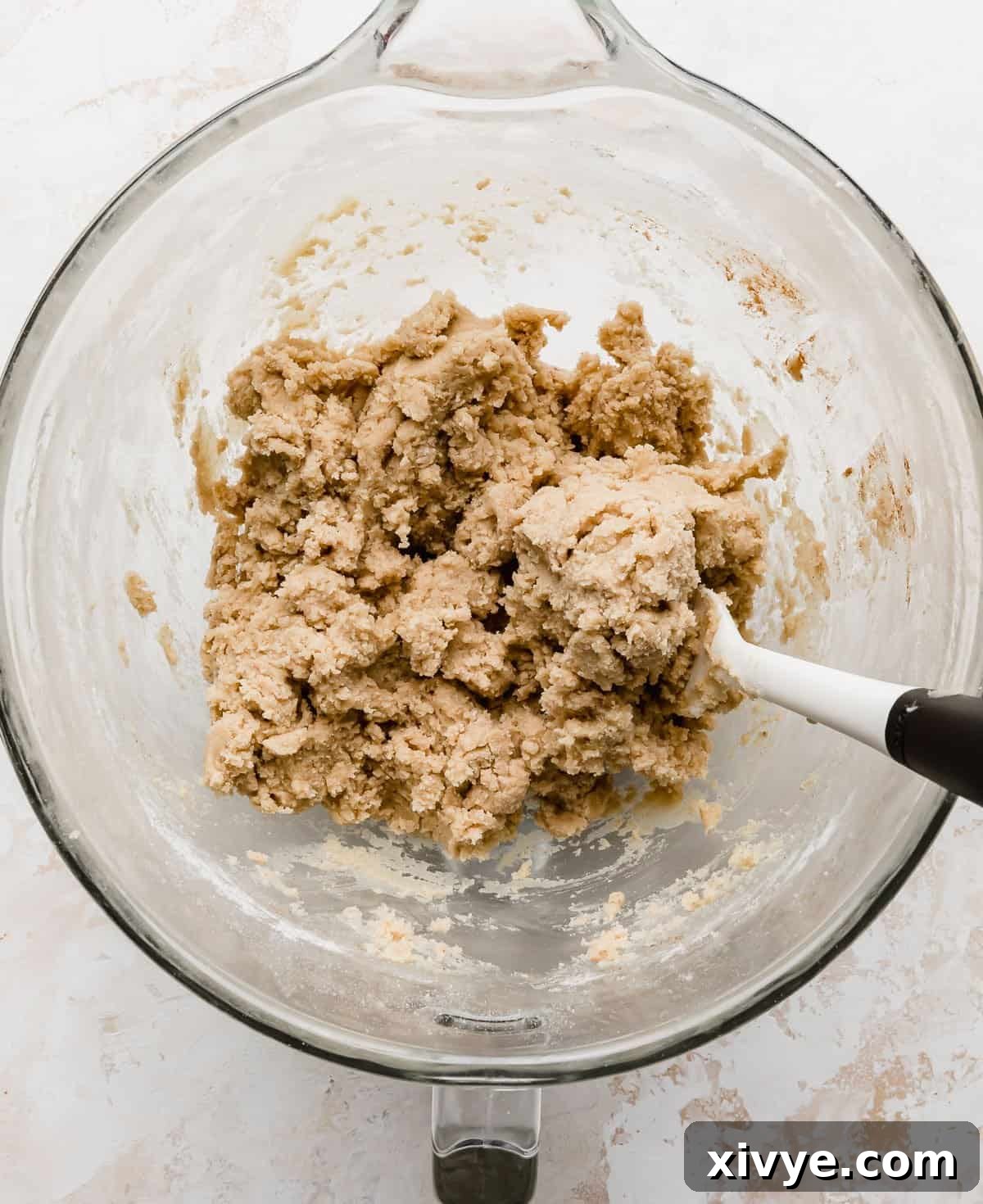 Homemade Crumbl Churro Cookie Perfection 4 Fluffy, pale yellow churro cookie dough rests in a clear glass bowl, showcasing its smooth texture against a pristine white background.