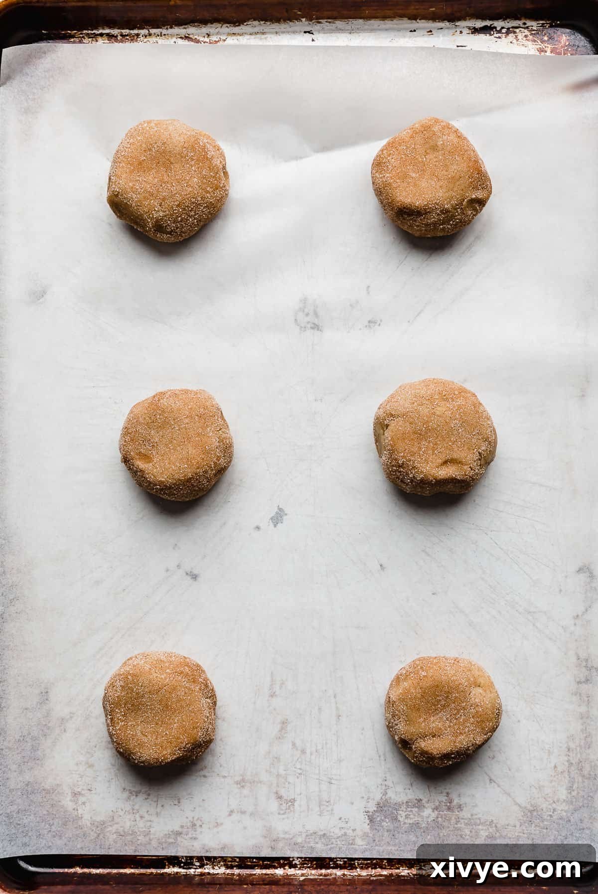 Homemade Crumbl Churro Cookie Perfection 6 Six perfectly portioned and cinnamon-sugar-coated churro cookie dough balls arranged neatly on a white parchment-lined baking sheet, ready for the oven.