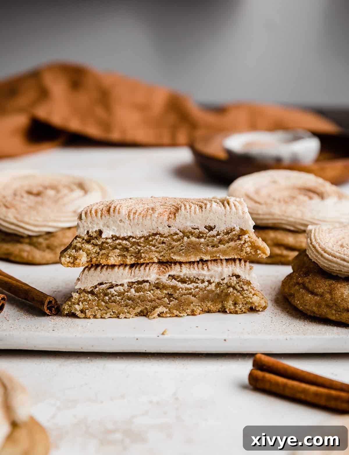 Homemade Crumbl Churro Cookie Perfection 9 A delectable churro cookie, perfectly cut in half, sits on a pristine white plate, revealing its soft, cinnamon-spiced interior and creamy frosting.