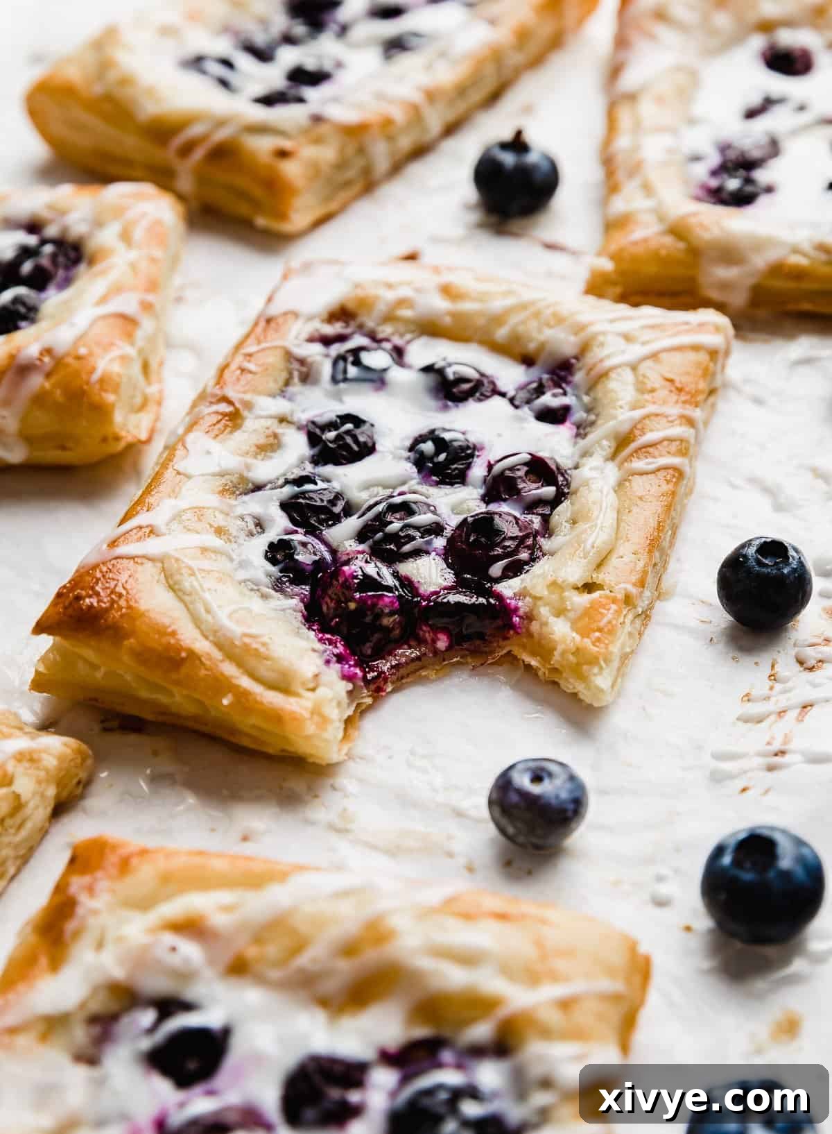 Flaky Blueberry Dream 11 A bite taken out of a Blueberry Danish with fresh blueberries near the pastry.