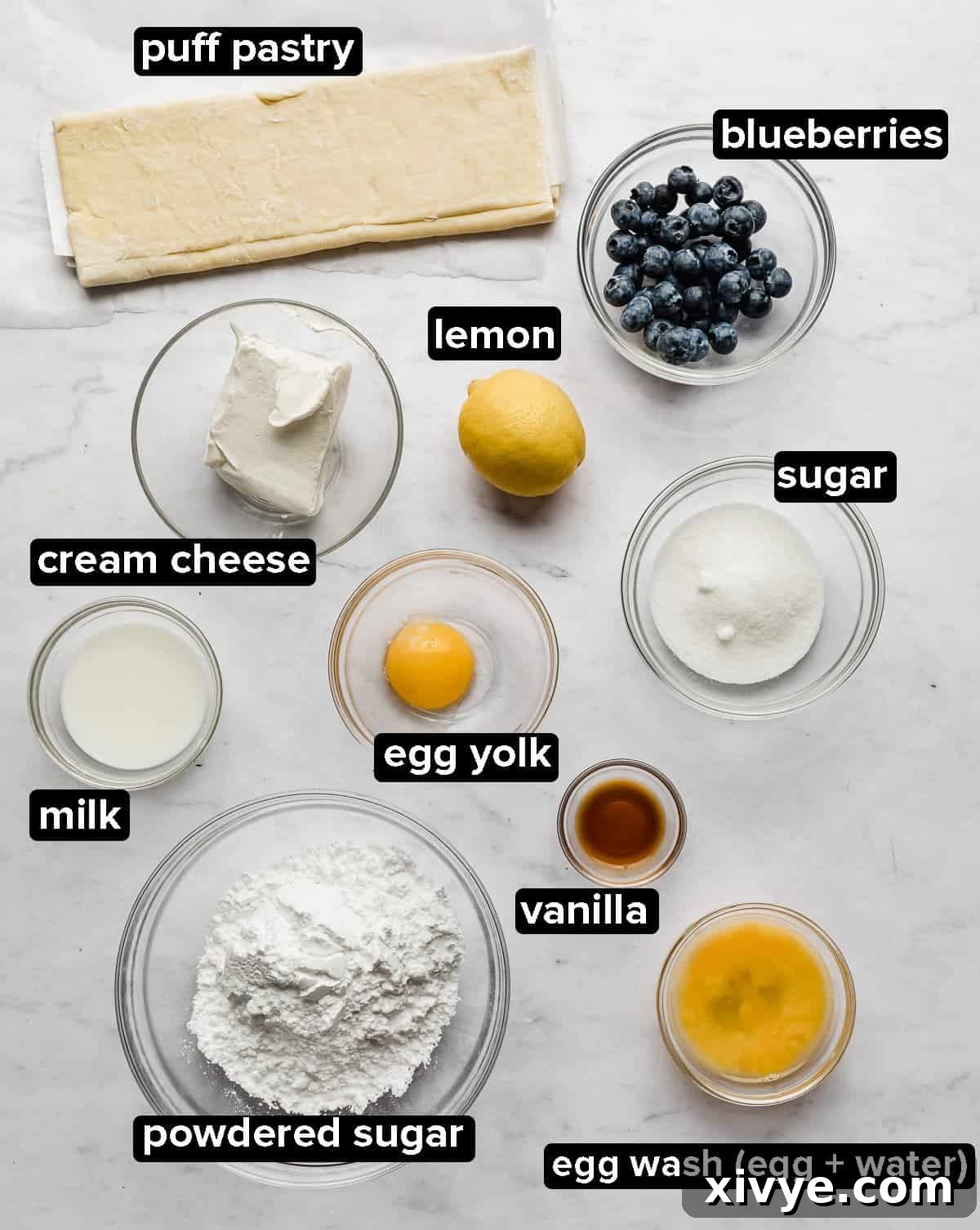 Flaky Blueberry Dream 3 Blueberry cream cheese danish ingredients separated into glass bowls on a white marble background.