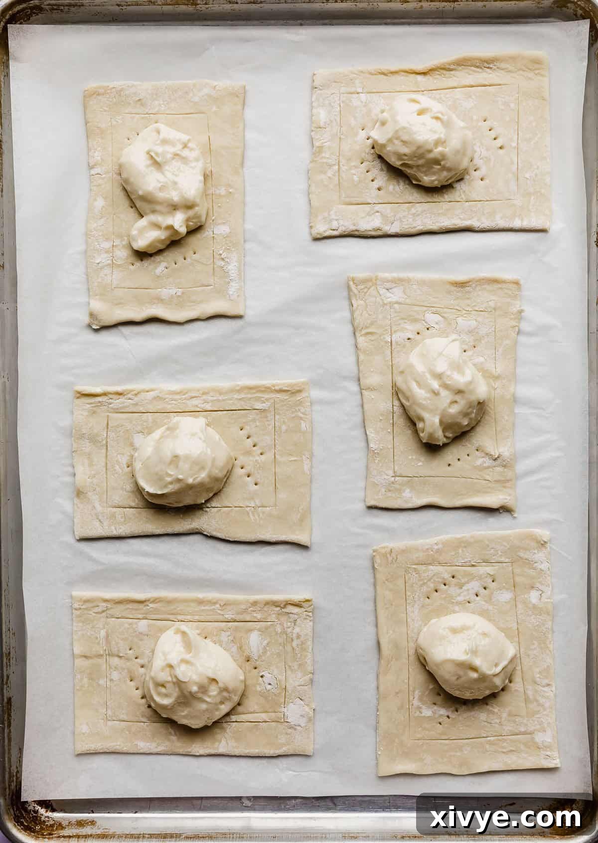 Flaky Blueberry Dream 6 A dollop of light yellow cream cheese mixture in the center of six rectangular puff pastry pieces on a baking sheet.