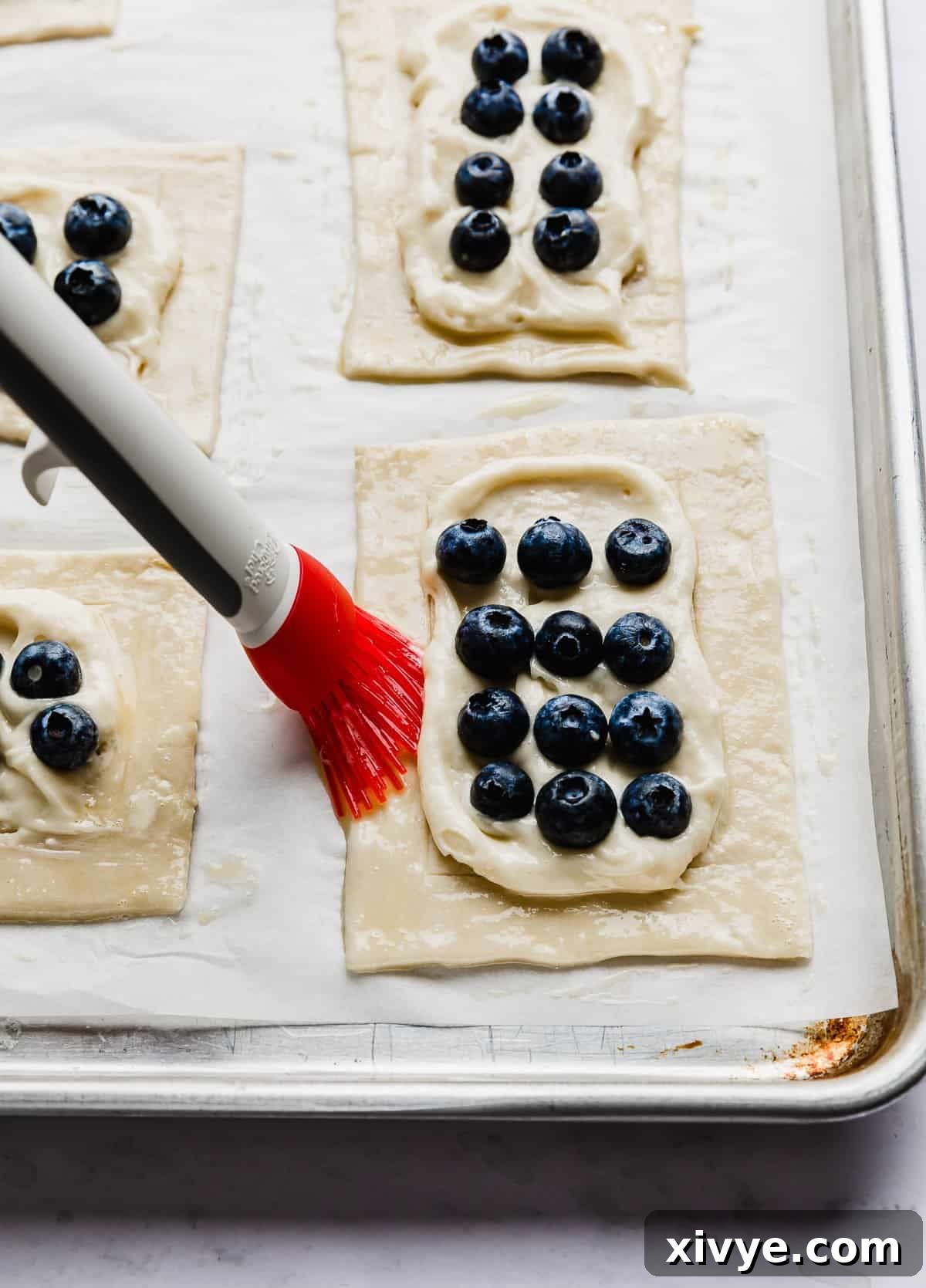 Flaky Blueberry Dream 8 A red bristle pastry brush going along the edges of a puff pastry square.