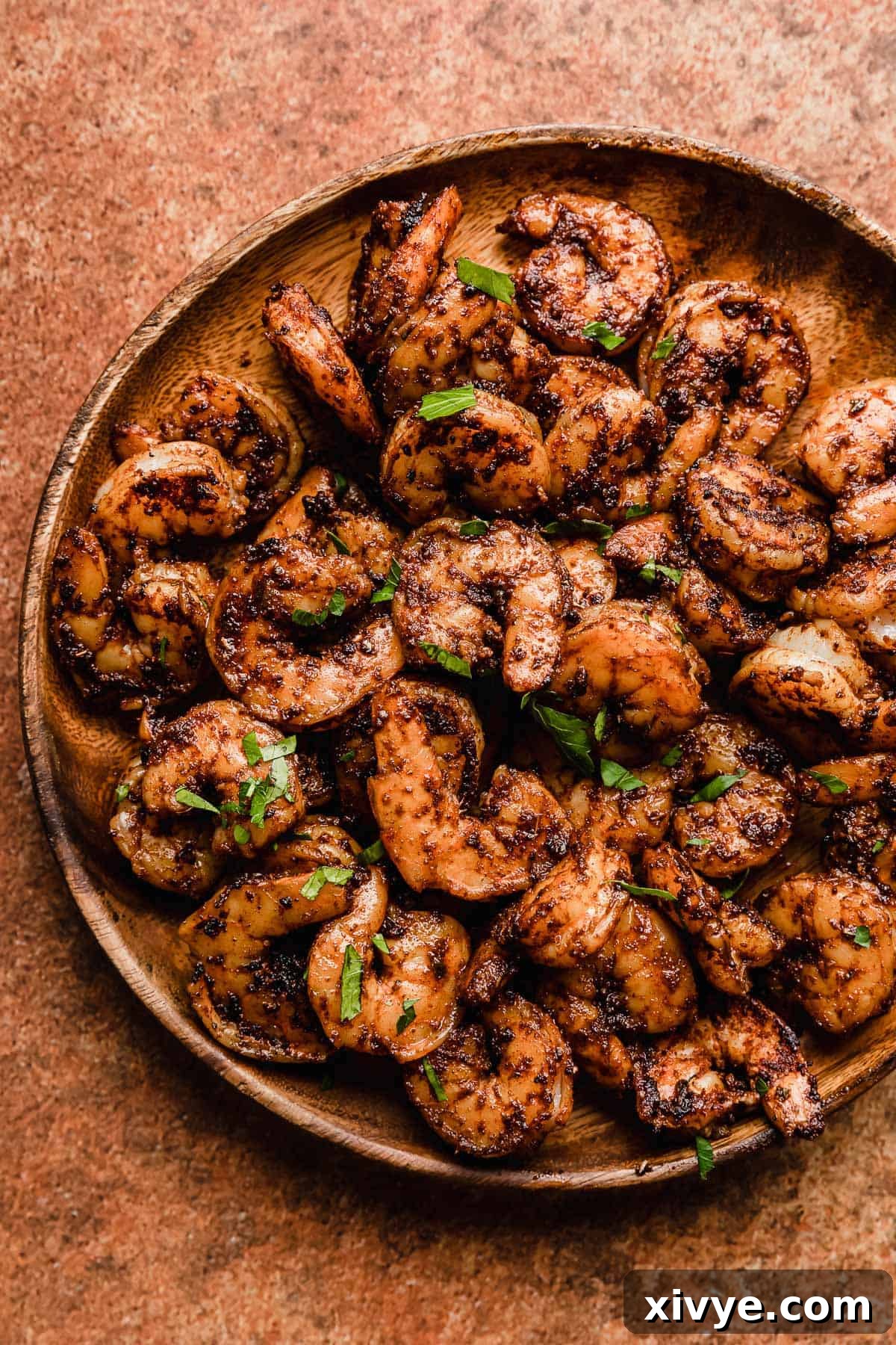 A wooden plate displaying perfectly cooked Blackened Shrimp, set against a warm, burnt orange background.