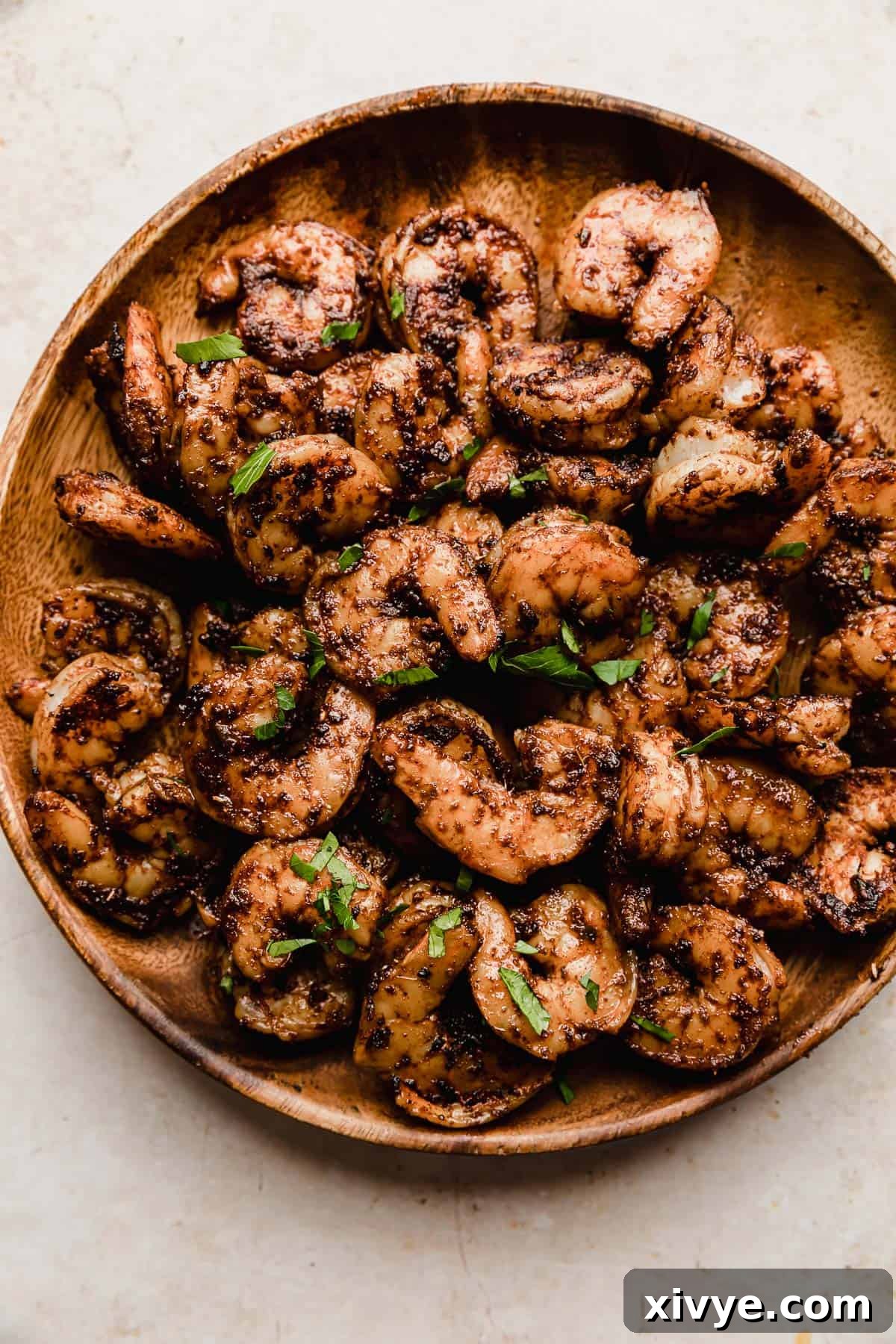 A wooden plate on a white background, elegantly presenting cooked Blackened Shrimp garnished with fresh chopped parsley.