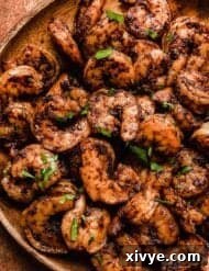 Close up photo of cooked Blackened Shrimp covered in spices and topped with fresh parsley, on a wood plate.