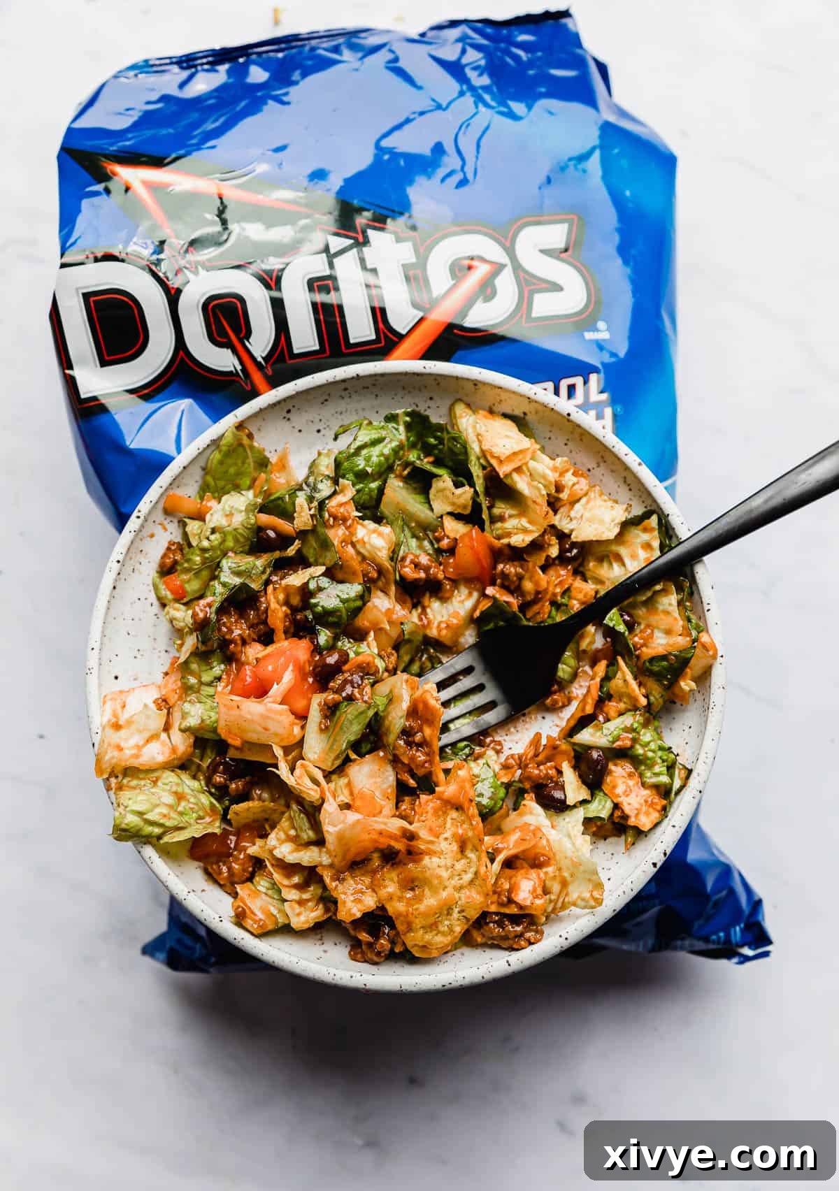 Ultimate Doritos Taco Salad 2 A vibrant Doritos Taco Salad served on a white plate, resting on a blue bag of Doritos Cool Ranch chips, showcasing its fresh ingredients and inviting appeal.