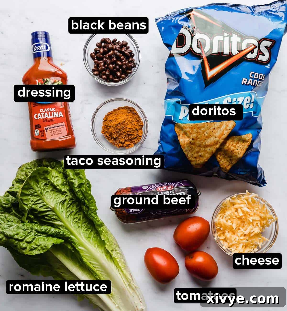 Ultimate Doritos Taco Salad 3 Key ingredients for Doritos Taco Salad laid out on a white background: ground beef, diced tomatoes, shredded cheese, Cool Ranch Doritos, crisp lettuce, and a bottle of Catalina dressing.