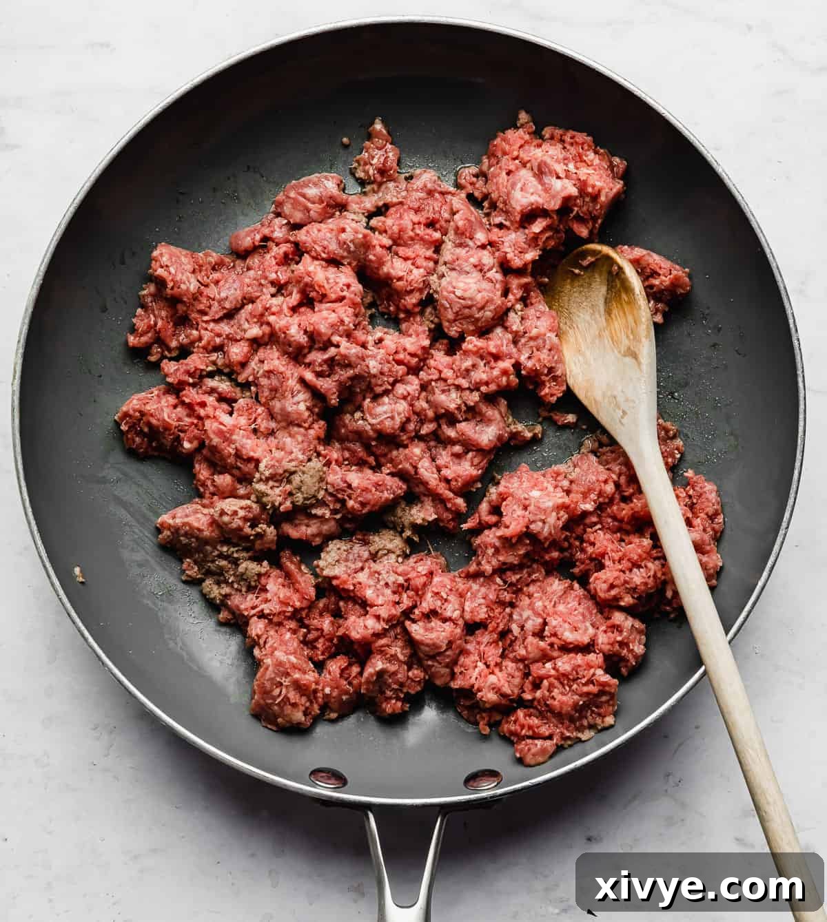 Ultimate Doritos Taco Salad 4 Raw ground beef cooking in a grey skillet on a white background, ready to be transformed into delicious taco meat.