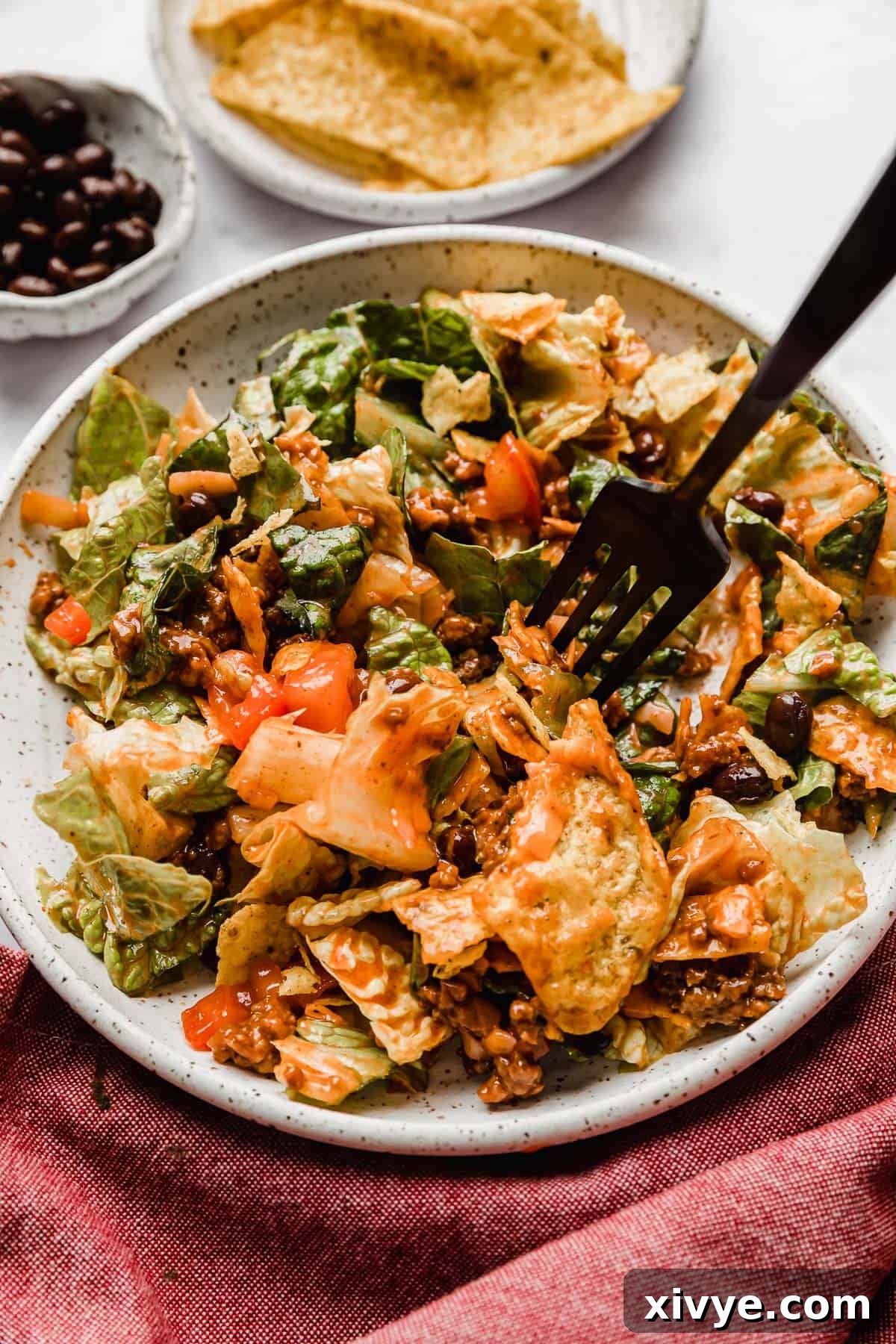 Ultimate Doritos Taco Salad 10 A close-up of Doritos Taco Salad with Catalina dressing, on a white plate with a black fork ready to scoop, highlighting its inviting textures and colors.