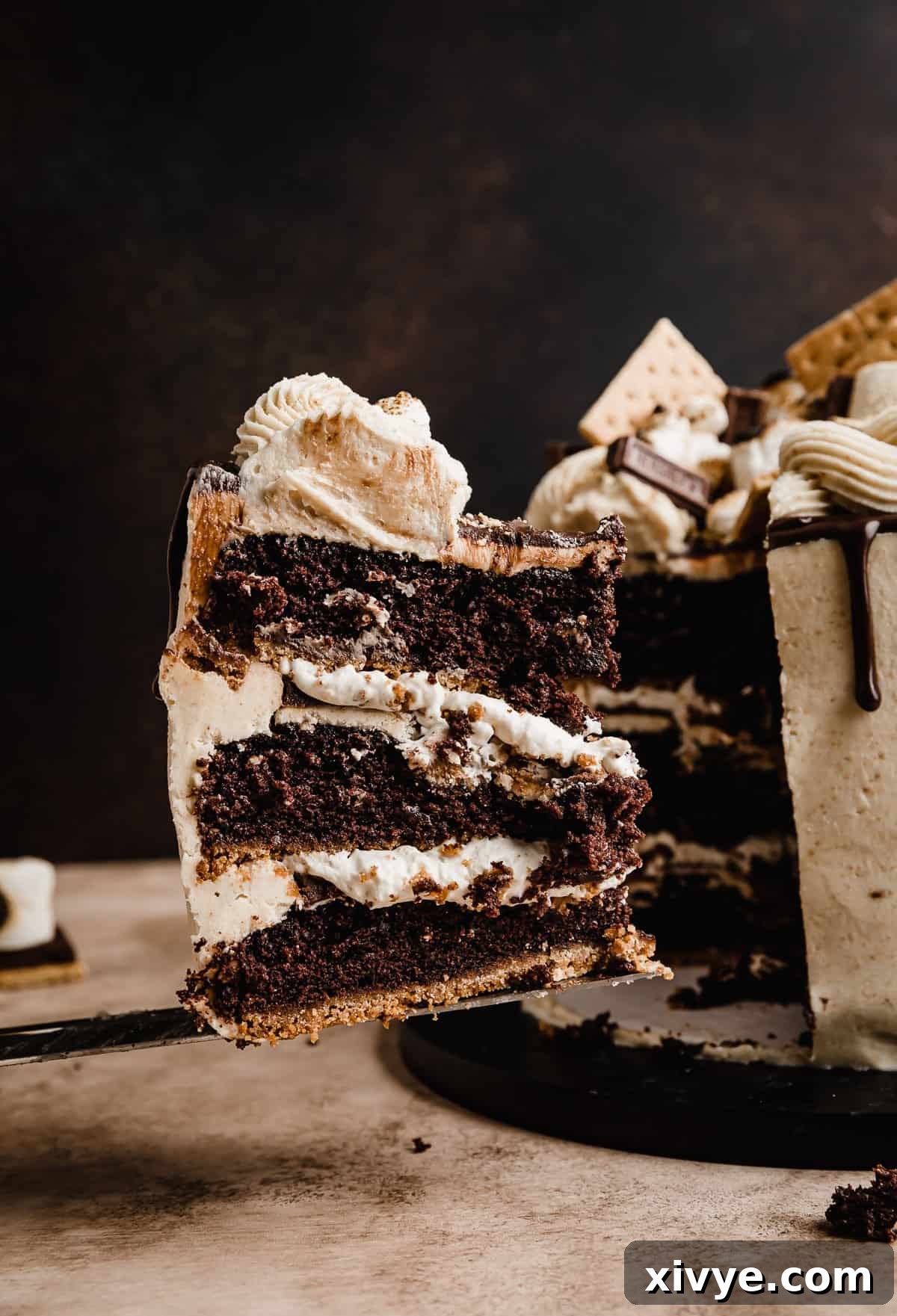 A slice of a S'mores three layer Cake balancing on a serving knife, in front of a brown background.