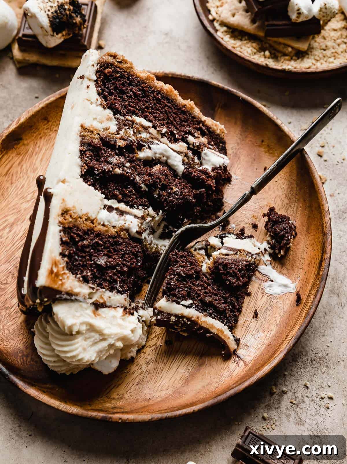 A slice of S'mores Cake on a brown wooden plate on a beige background.