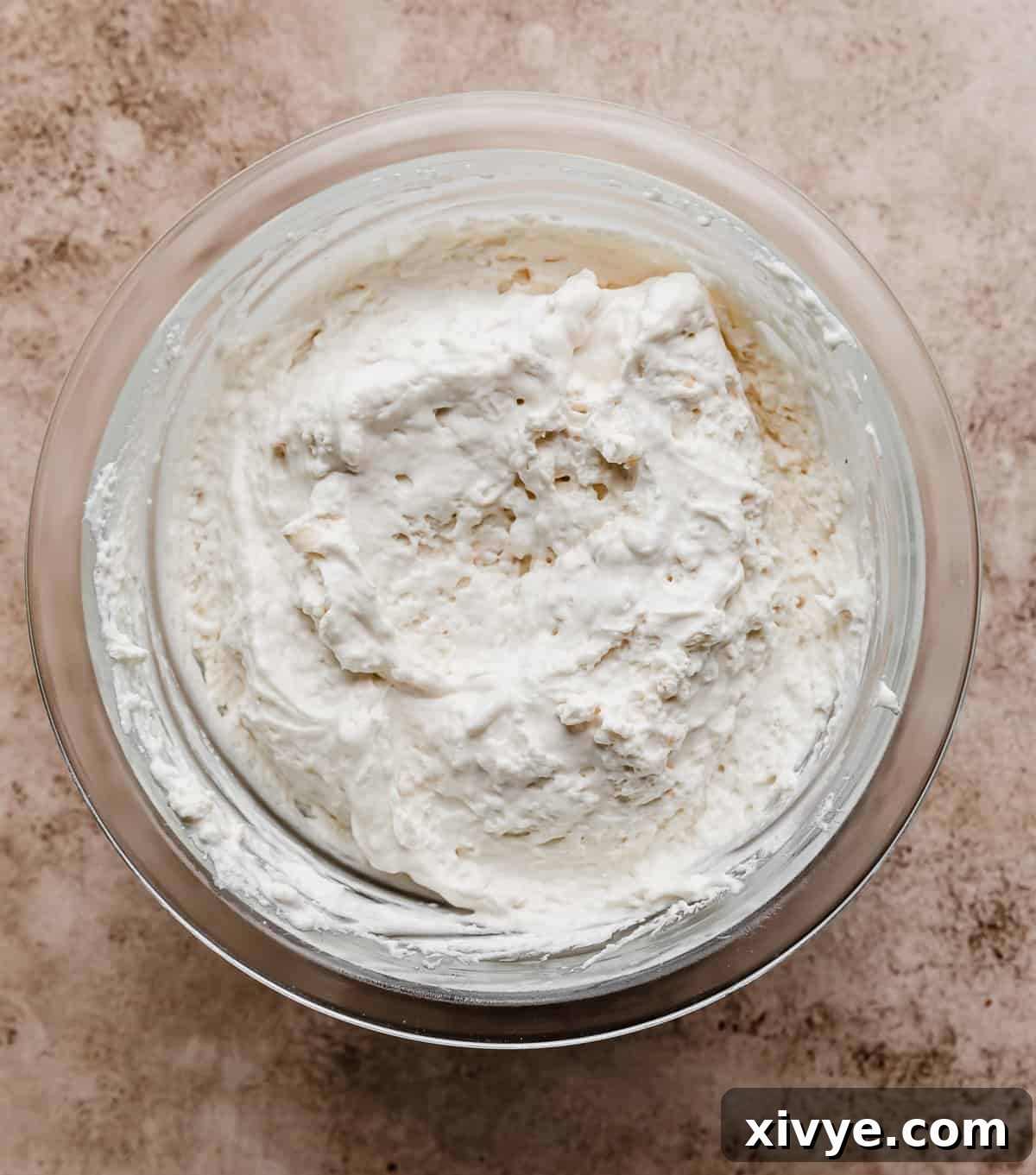 Toasted marshmallow whipped cream in a glass bowl on a beige textured background.