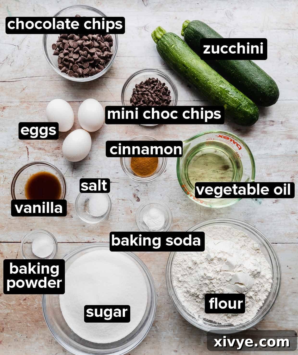 Ingredients used to make chocolate chip zucchini bread on a light wooden background.