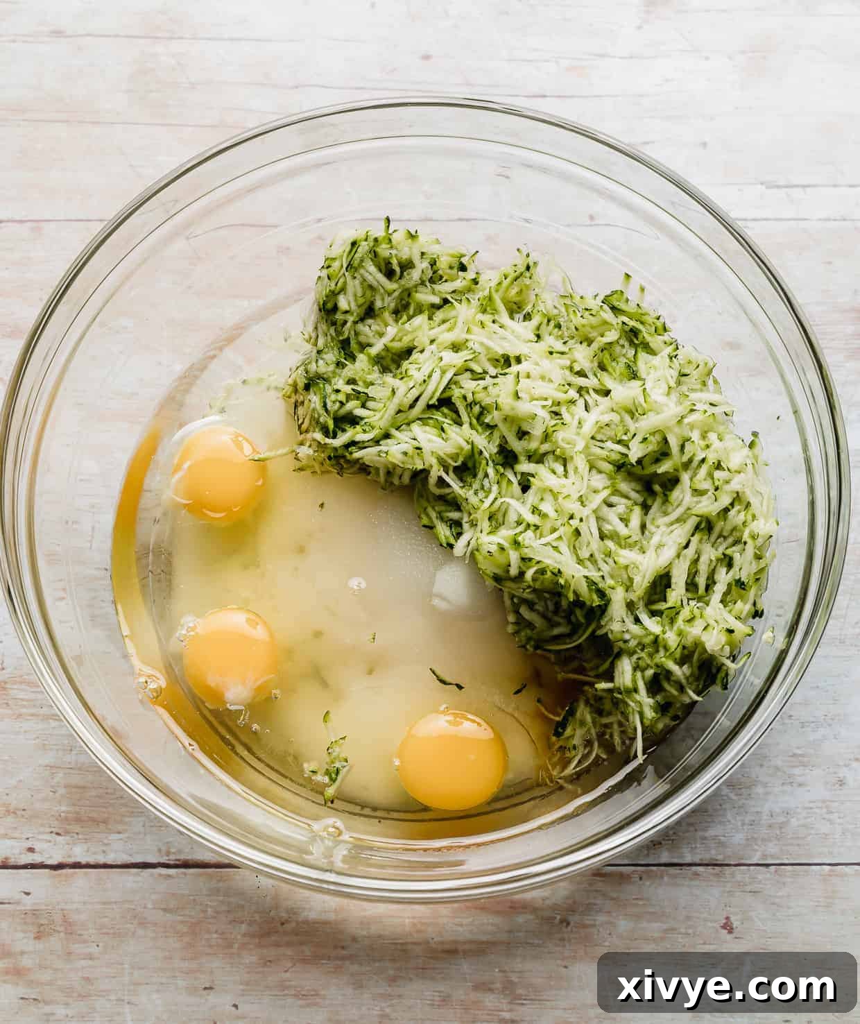 Shredded zucchini, eggs, sugar, and vanilla in a glass bowl.