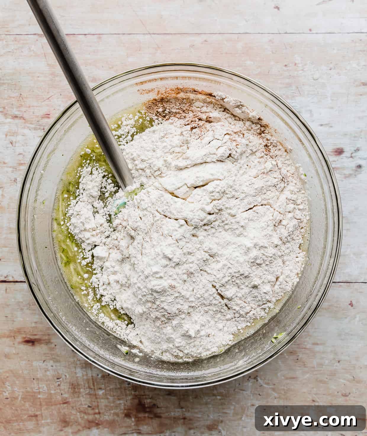A glass bowl with flour poured overtop of green batter.