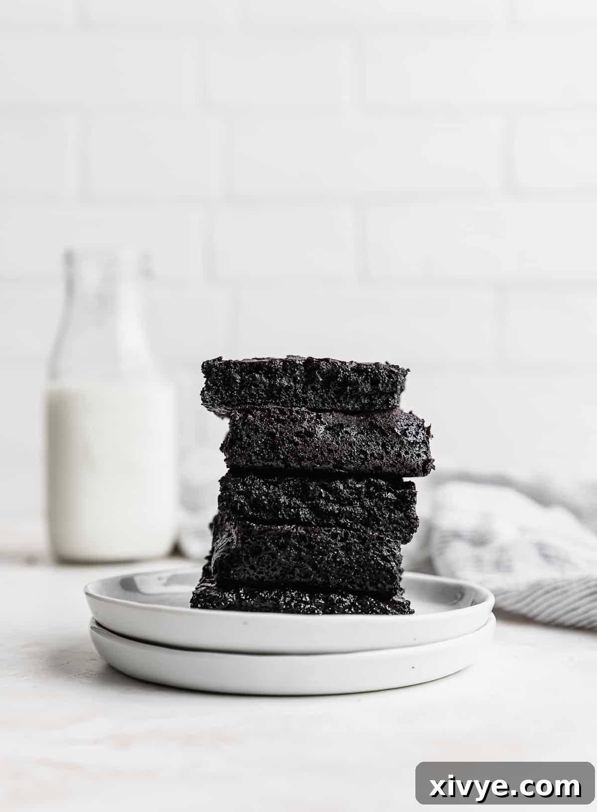 Ultimate Blackout Brownies 8 Five black cocoa brownie squares stacked on top of each other, on two white plates against a white brick background.