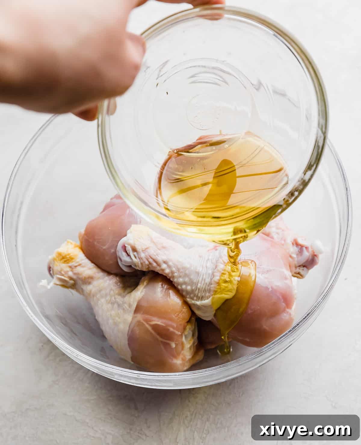 Crispy Air Fryer Drumsticks 4 Olive oil being poured overtop chicken drumsticks that are in a glass bowl.