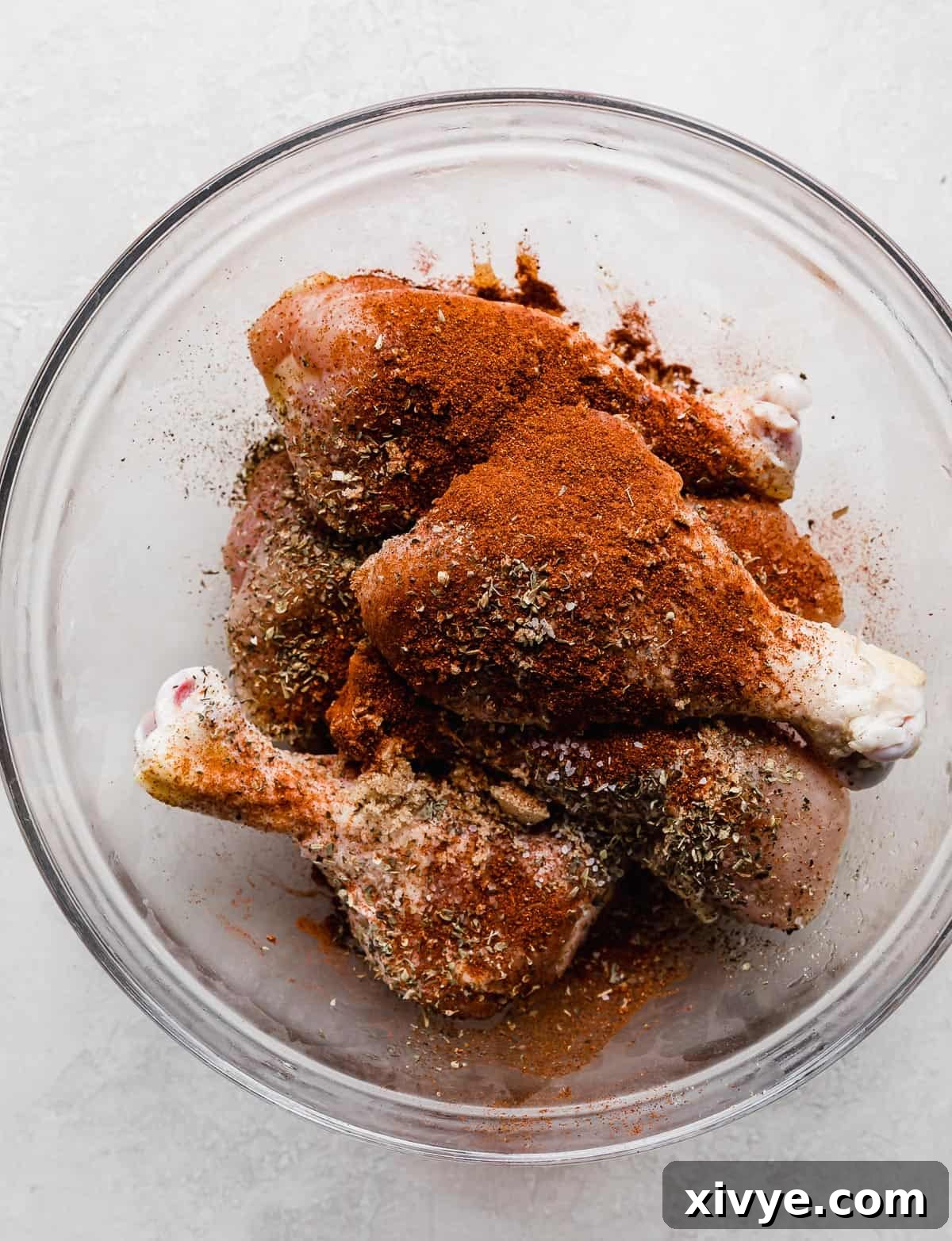 Crispy Air Fryer Drumsticks 5 Dried spices such as paprika, Italian seasoning, salt, and pepper sprinkled overtop raw chicken legs that are in a glass bowl.