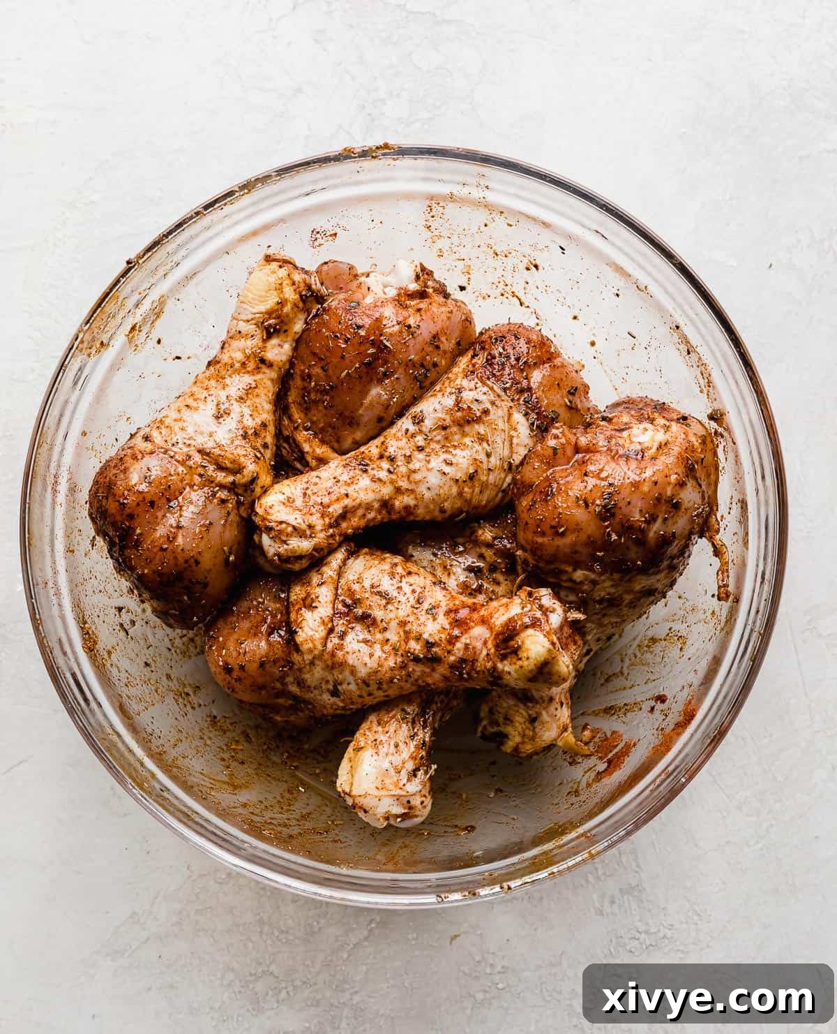 Crispy Air Fryer Drumsticks 6 Raw chicken legs in a glass bowl that have been tossed with dried spices.