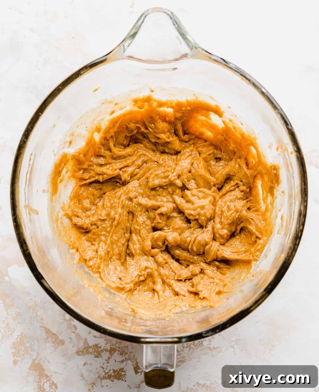 Smooth, pale orange pumpkin chocolate chip cookie dough, without the chocolate chips yet, in a glass stand mixer bowl, perfectly mixed.