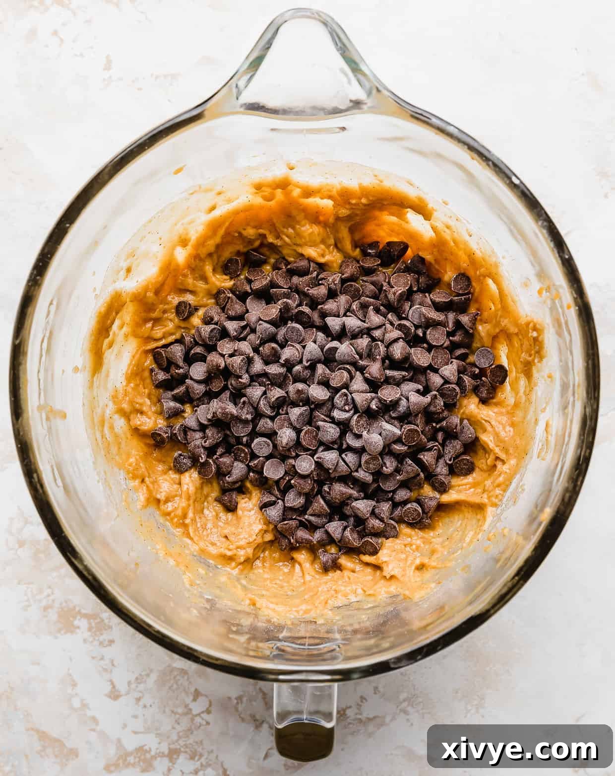 A generous sprinkling of chocolate chips resting atop pumpkin chocolate chip cookie dough batter in a glass bowl, ready to be gently folded in.