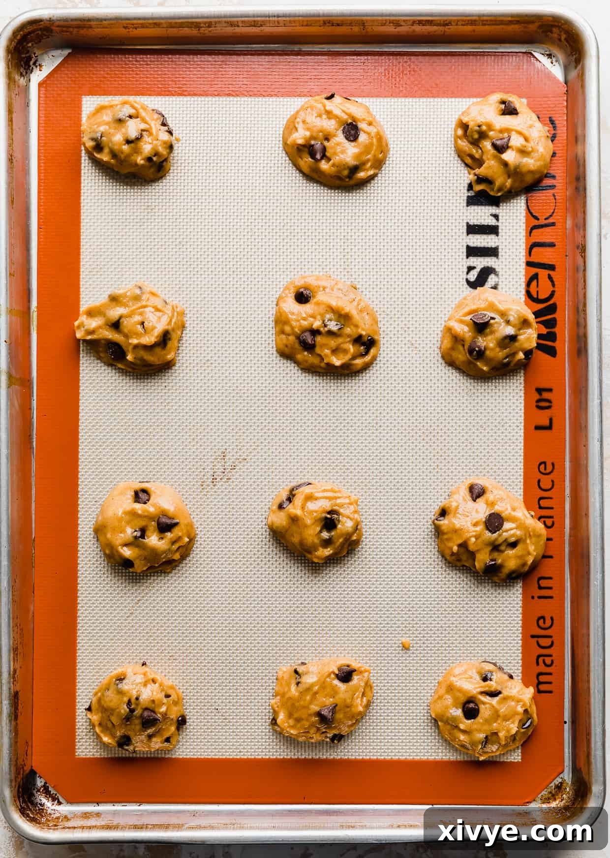 Unbaked pumpkin chocolate chip cookie dough balls neatly arranged and spaced out on a baking sheet lined with parchment paper, perfectly ready for the oven.